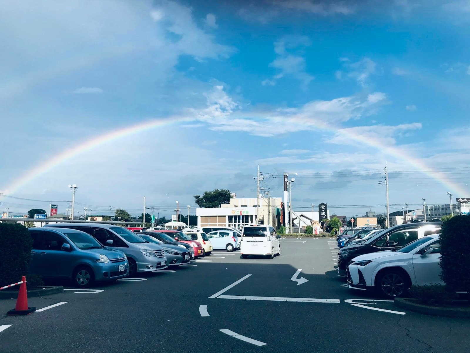 Rainbow over parking lot filled with cars on sunny day with blue sky and white clouds