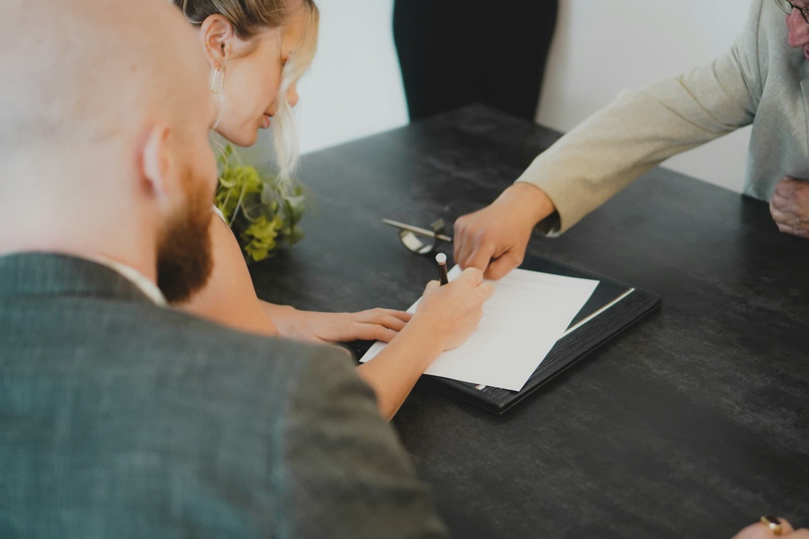 Woman in a light blazer pointing out documents to a bearded man across the table