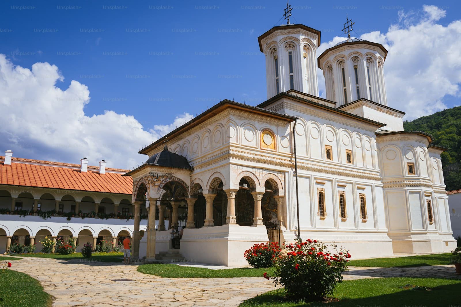 White Orthodox monastery with twin bell towers, red tile roof, and arched colonnade under blue sky