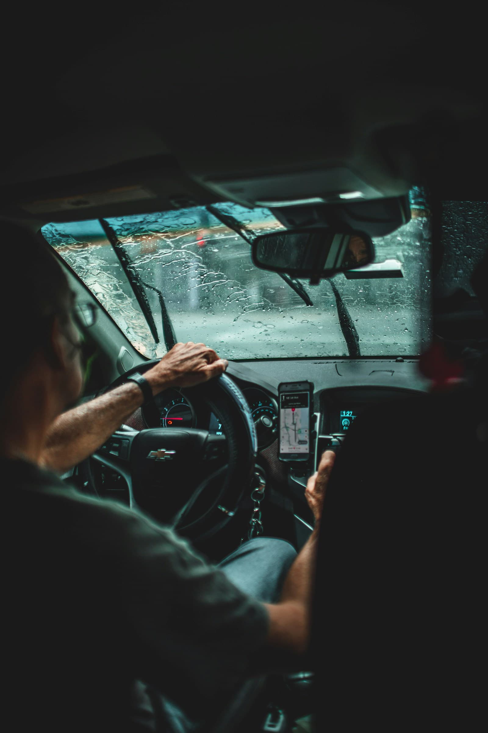 Driver at night in heavy rain with a dash-mounted phone and rain streaking the glass