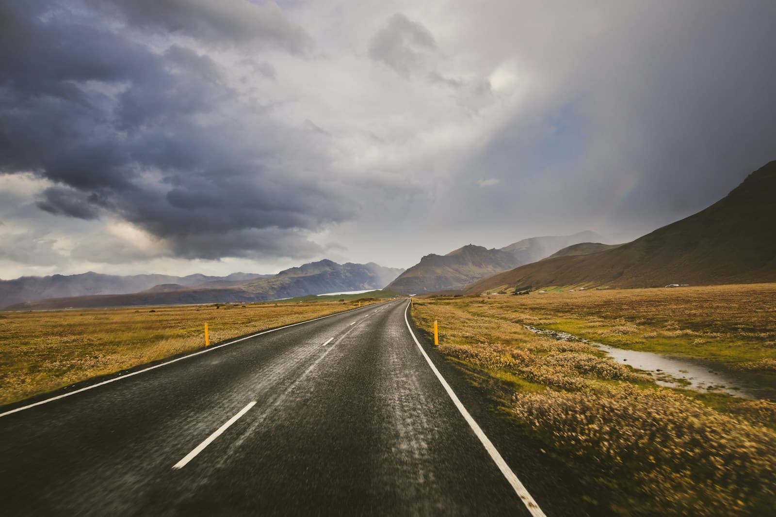 Straight empty road running toward distant mountains under a stormy sky