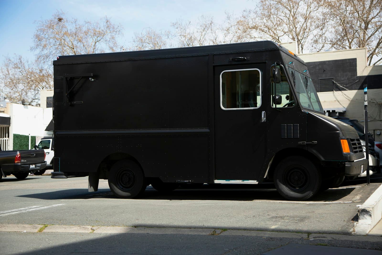 Dark armored security truck parked on a street among bare winter trees