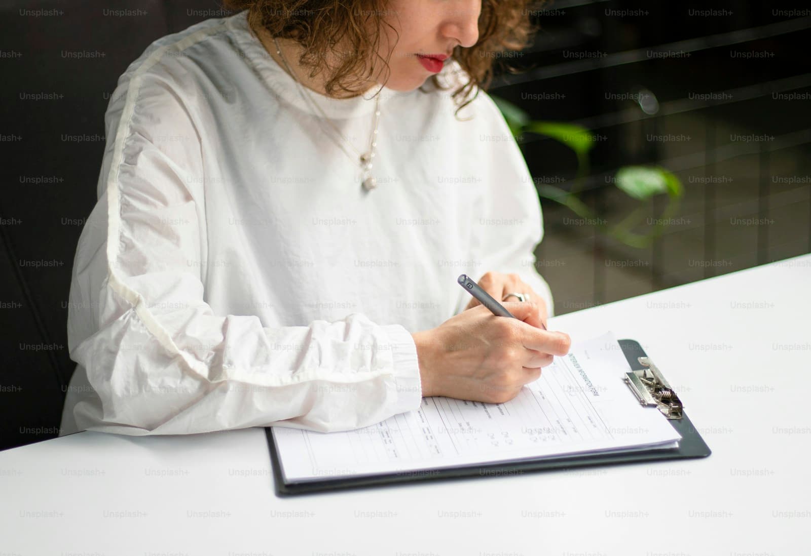 Woman in white shirt writing in notebook at white desk in modern office setting