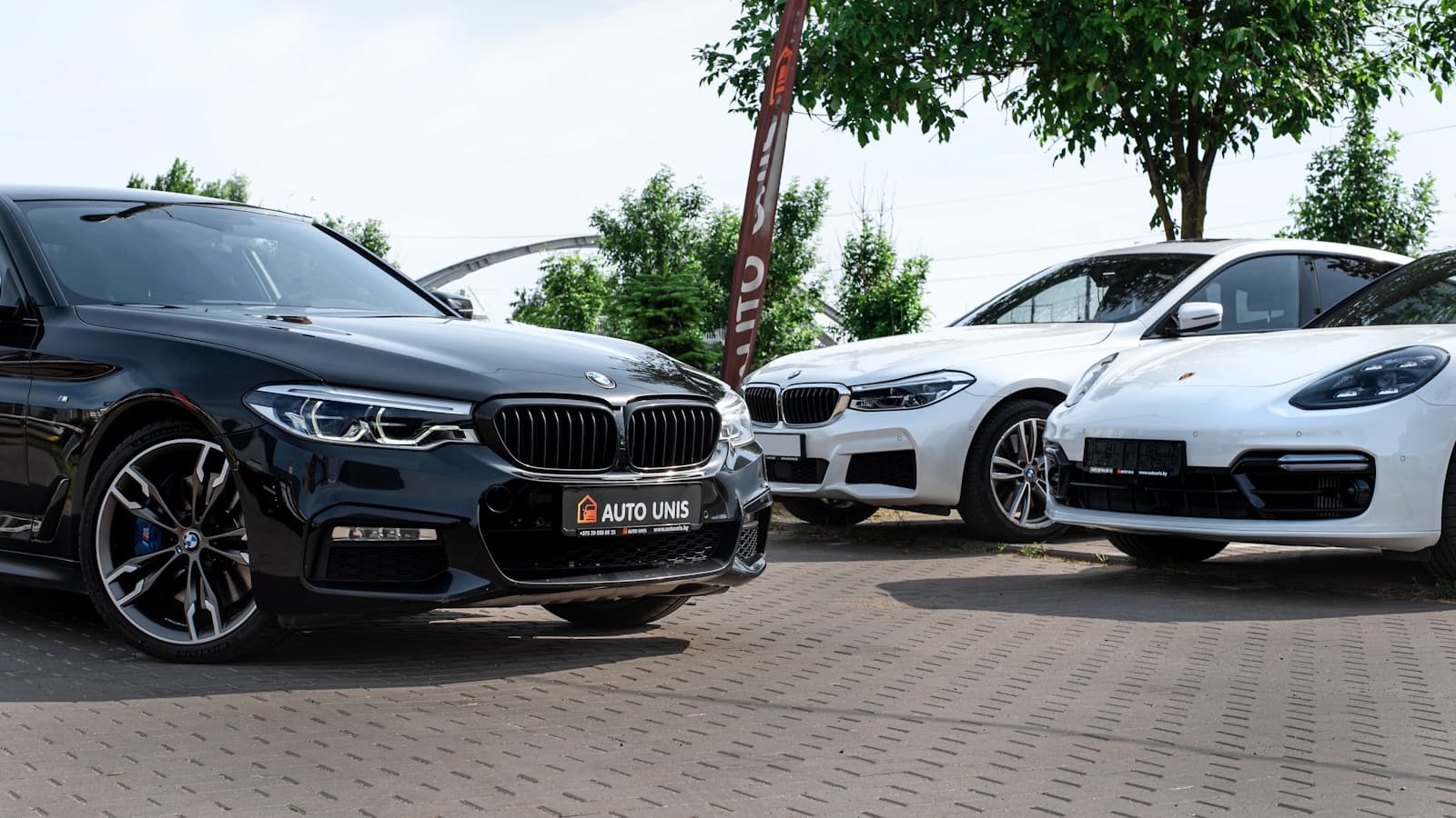 Three luxury cars on a dealership lot with a dark BMW sedan in the foreground