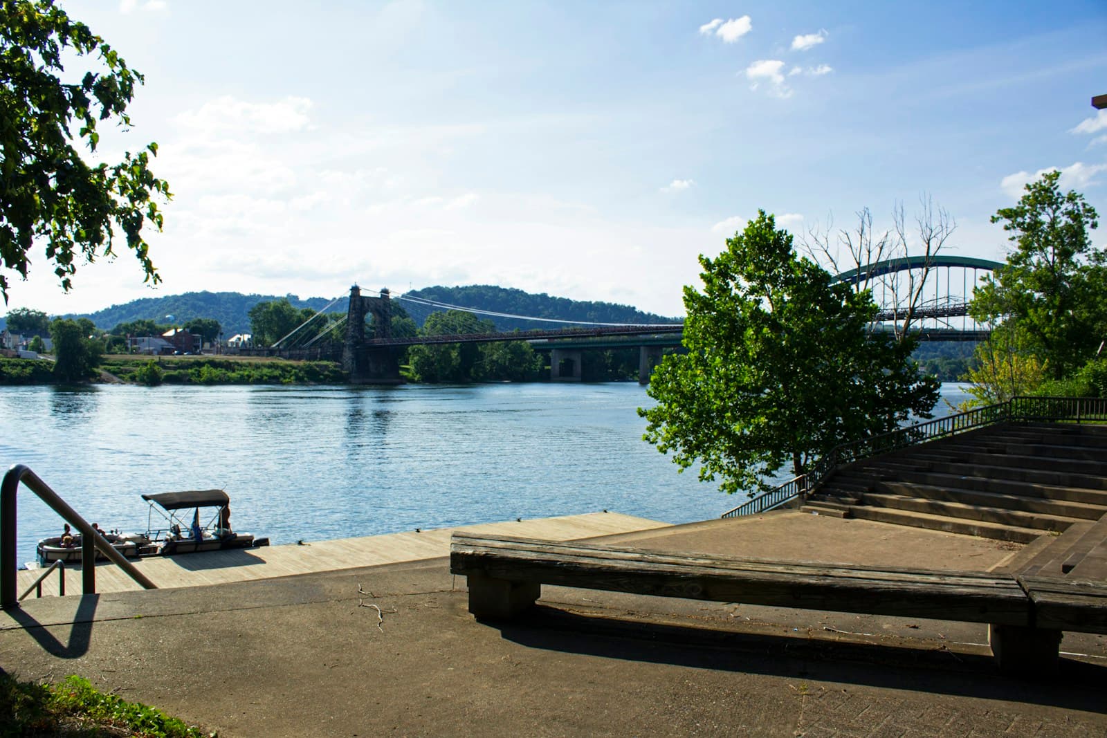 Wooden dock extending into calm water with trees and hills in background under blue sky