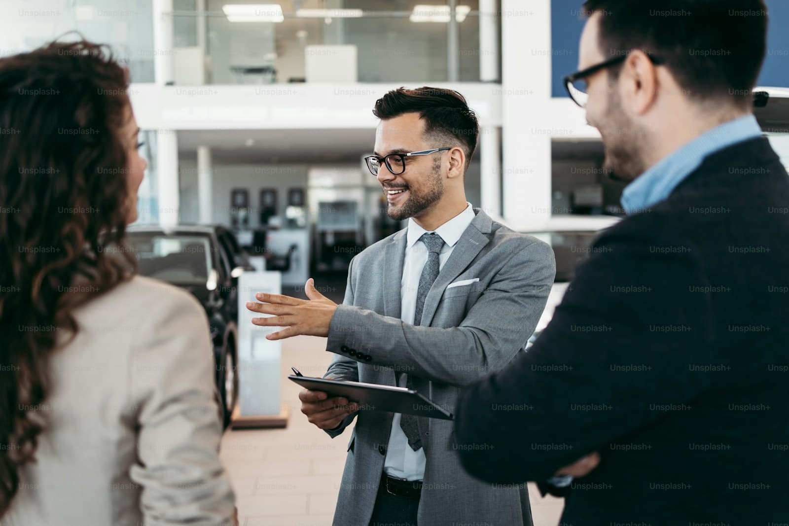 Man in a grey suit gesturing while talking with two people in a showroom