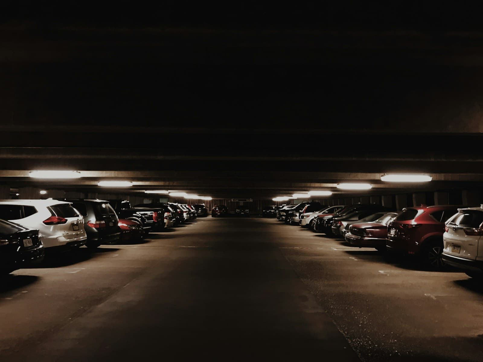 Underground parking garage with cars parked along both sides of a dimly lit driving lane