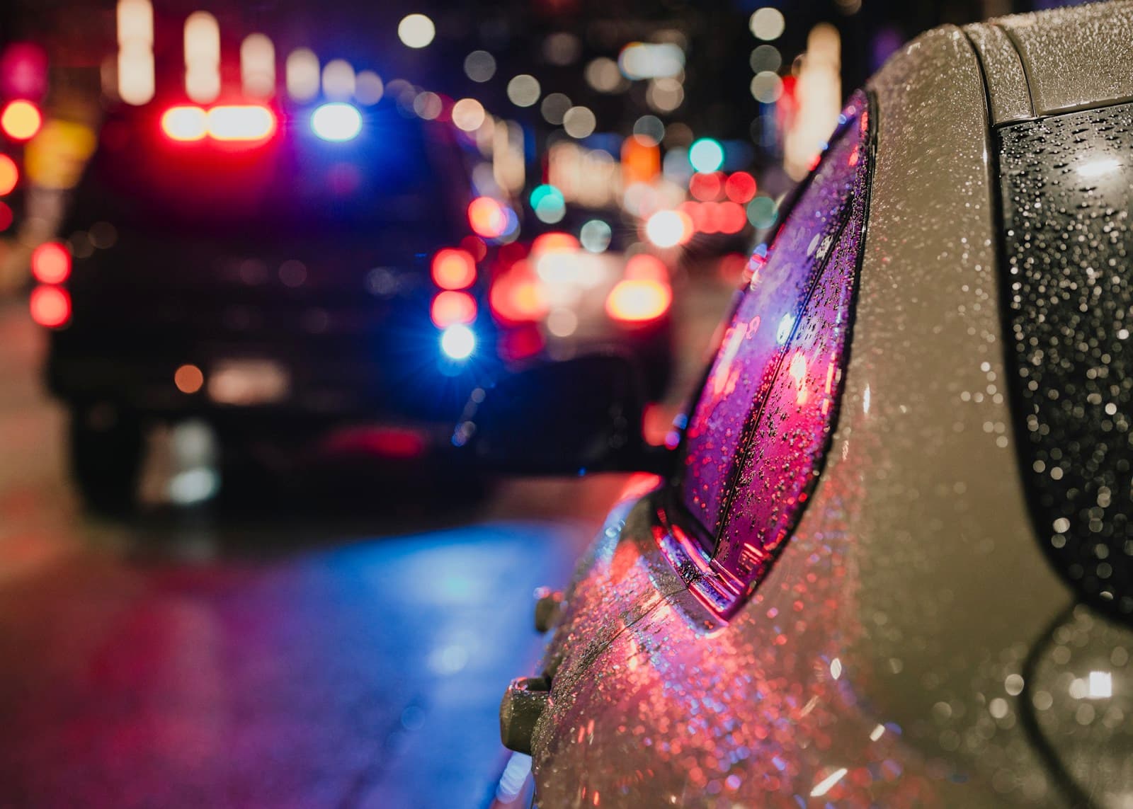 Wet car surface with colorful city lights reflecting at night, rain droplets visible with blurred urban background