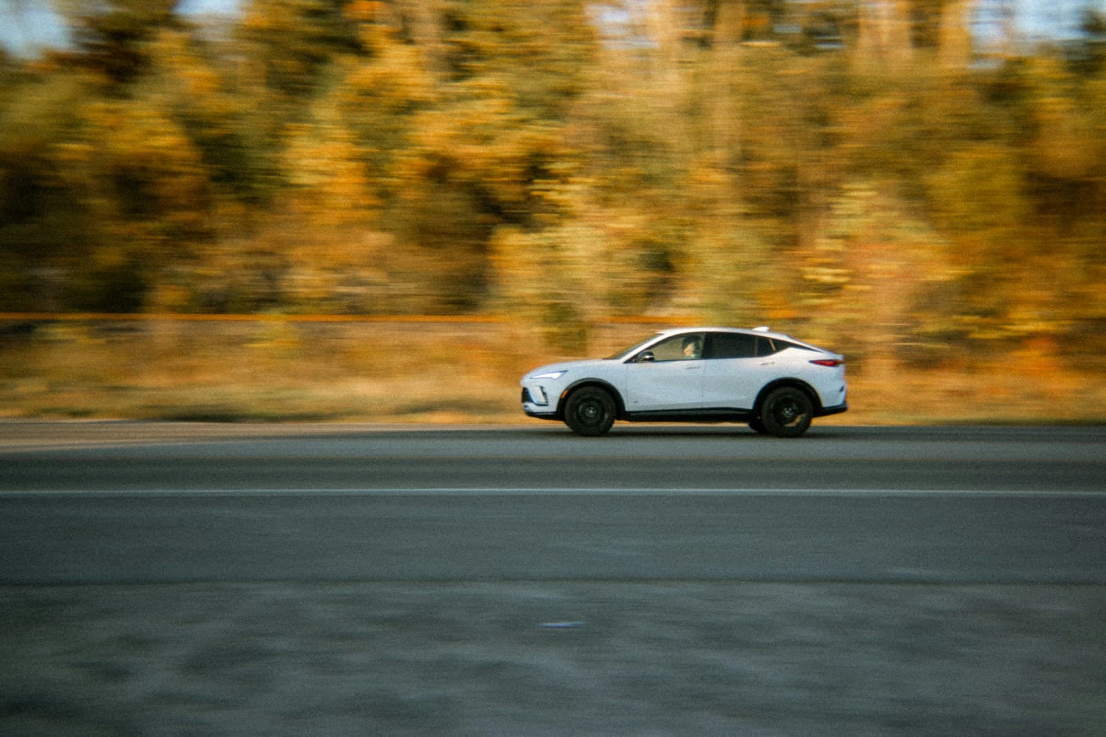 White SUV traveling a road lined with golden autumn foliage, captured with motion blur