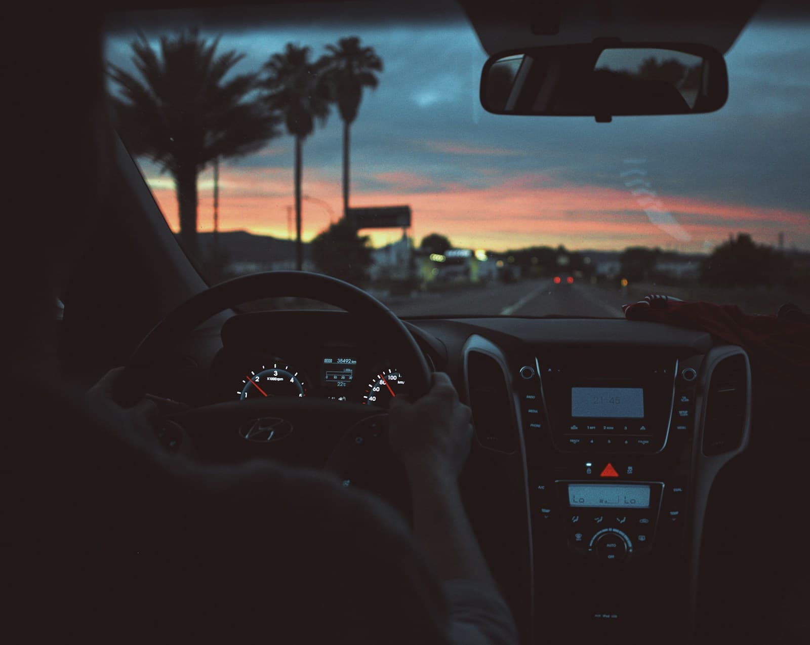 Car interior view at sunset with palm trees silhouetted against colorful sky through windshield