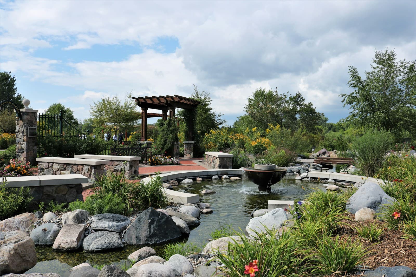 Japanese garden with wooden bridge over pond, surrounded by rocks, plants and pergola structure