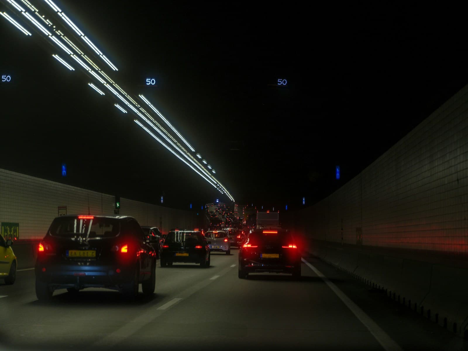 Traffic congestion in a lit highway tunnel at night with cars showing brake lights