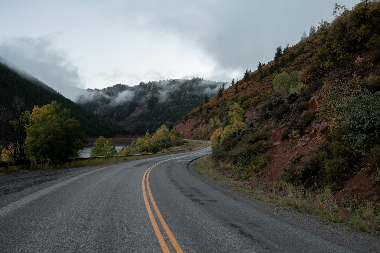 Curved two-lane mountain highway through autumn hillsides with mist over distant peaks