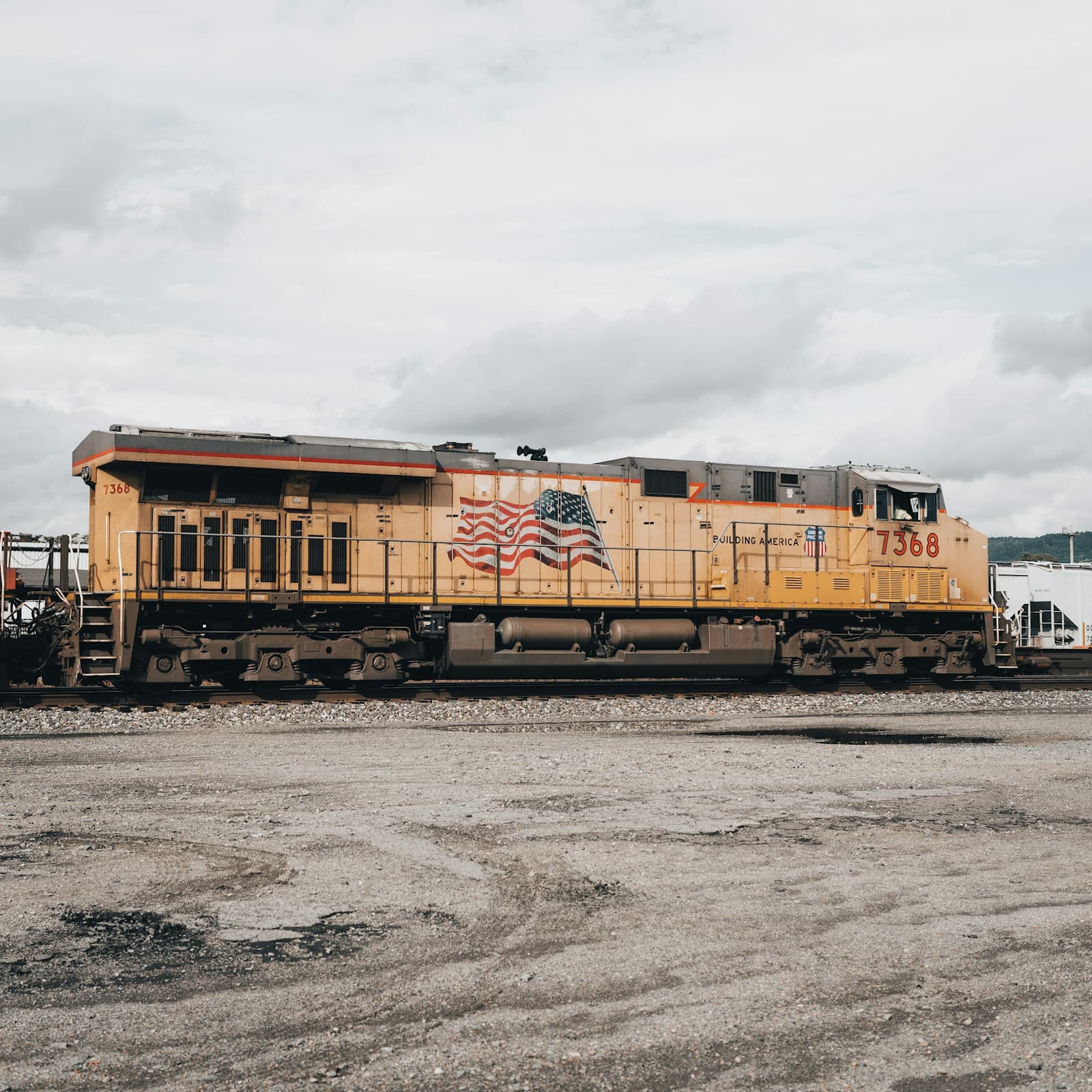 Yellow and orange diesel locomotive #7300 on railroad tracks in industrial rail yard under cloudy sky