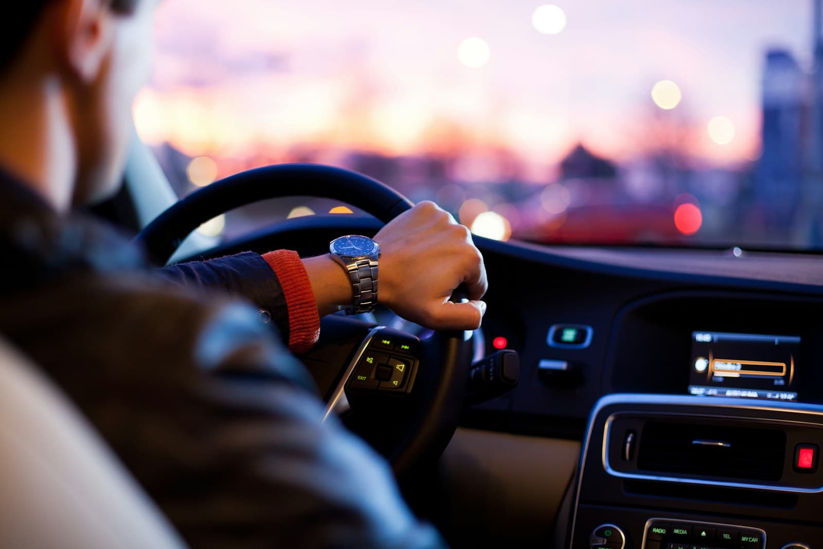 Driver at the wheel at twilight with city lights blurred beyond the windshield