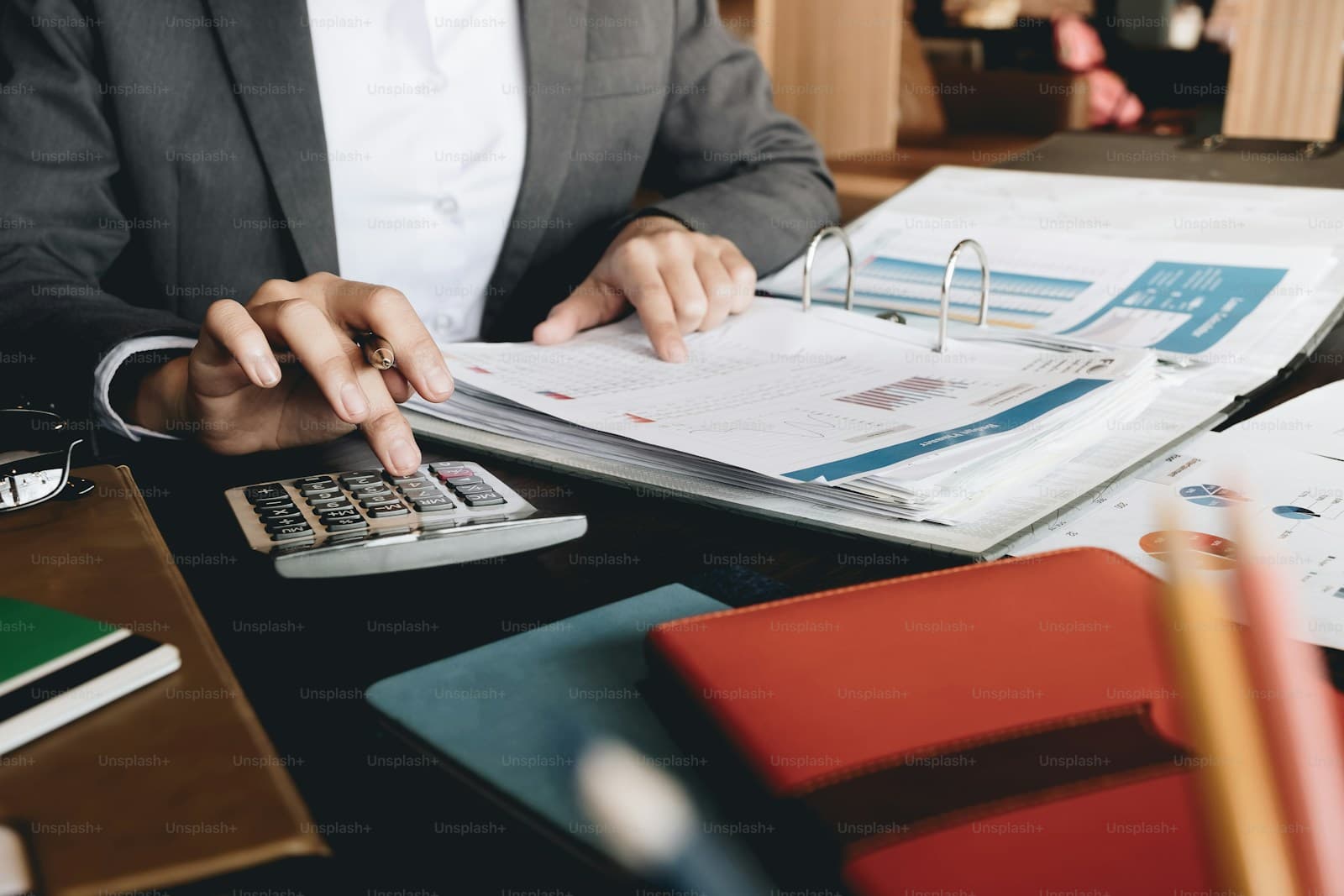 Person in a gray blazer using a calculator while reviewing charts in an open binder