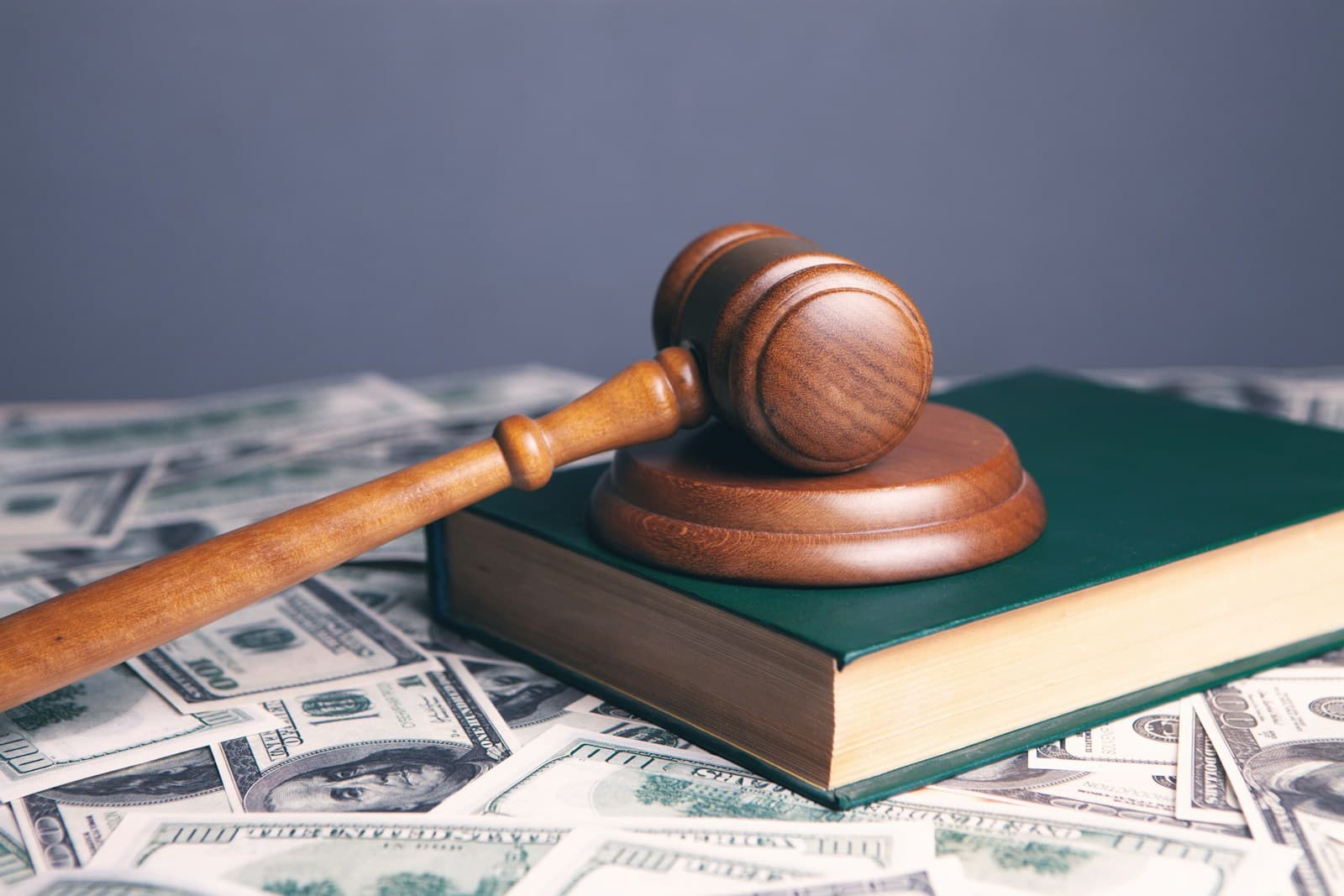 Wooden judge's gavel on green law book surrounded by scattered dollar bills