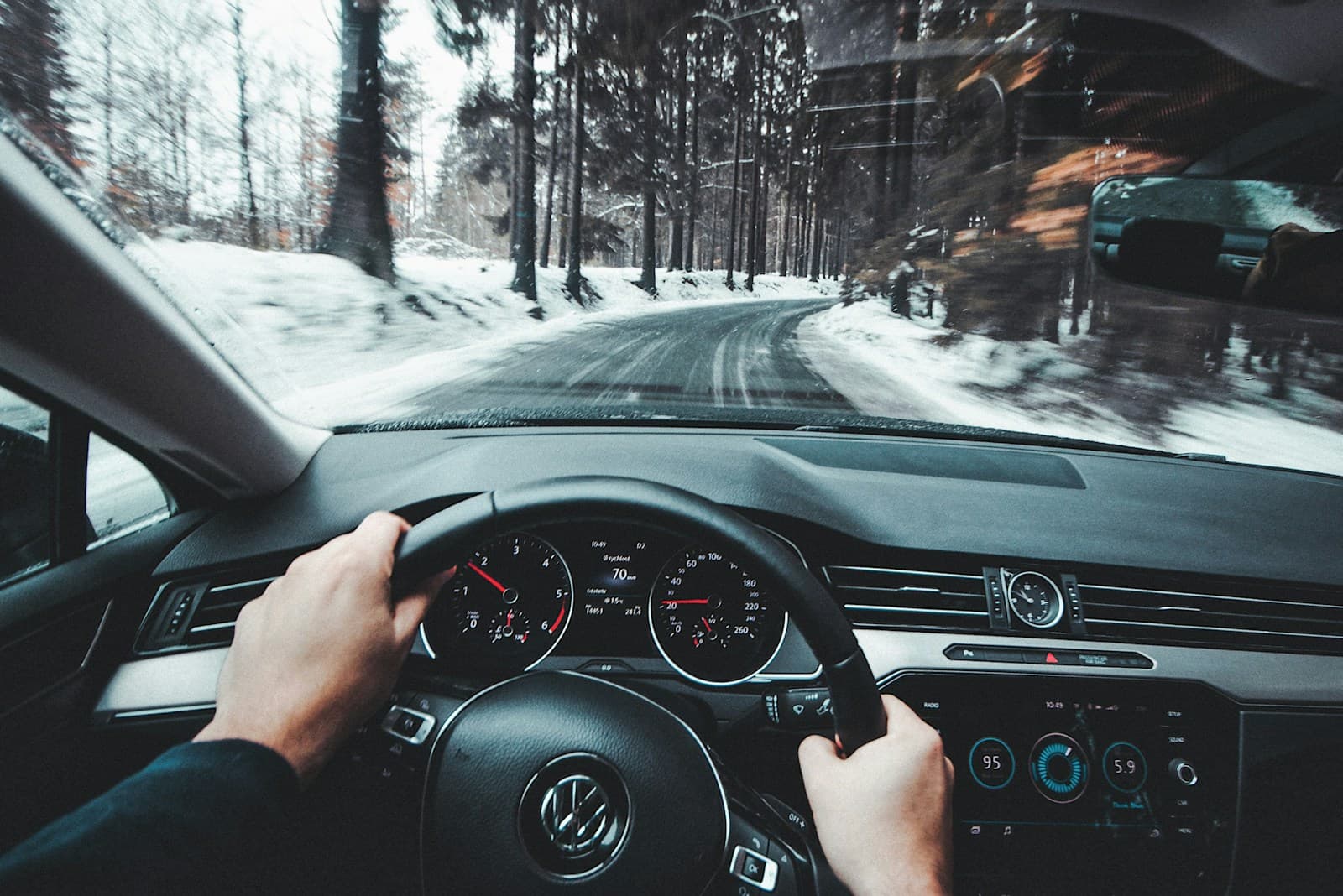 Driver at the wheel of a Volkswagen on a snowy tree-lined winter road