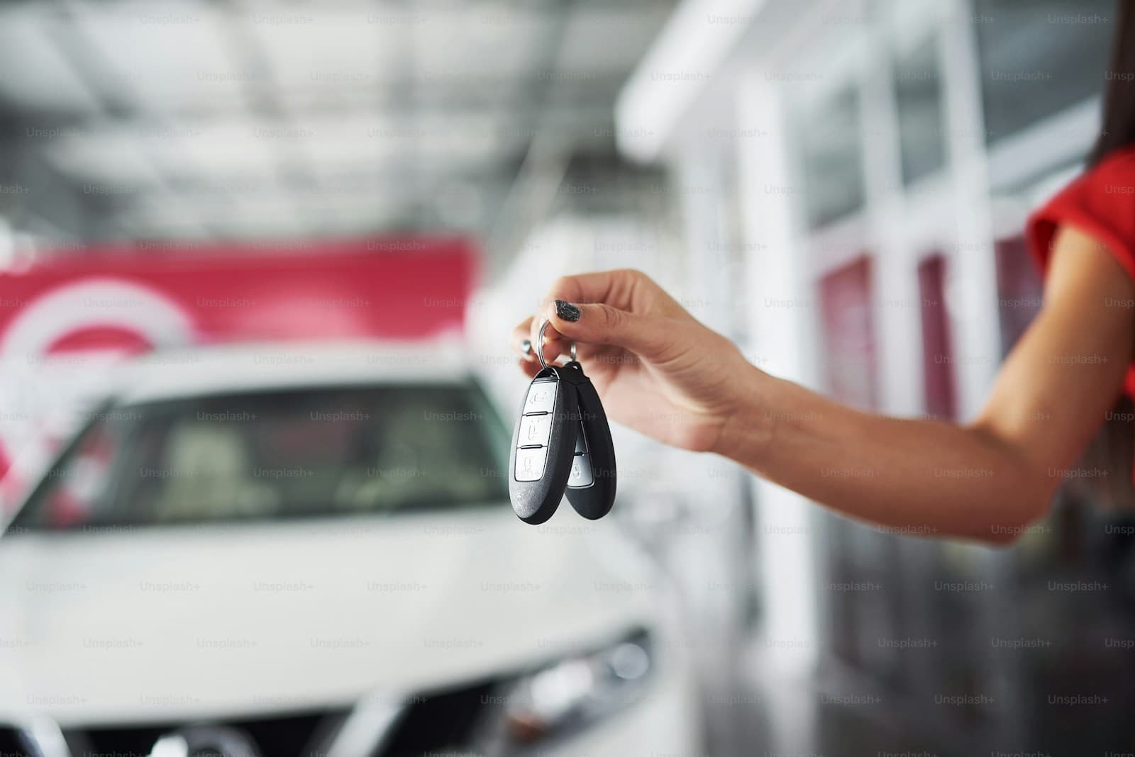 Hand offering a set of car keys with a white vehicle blurred behind