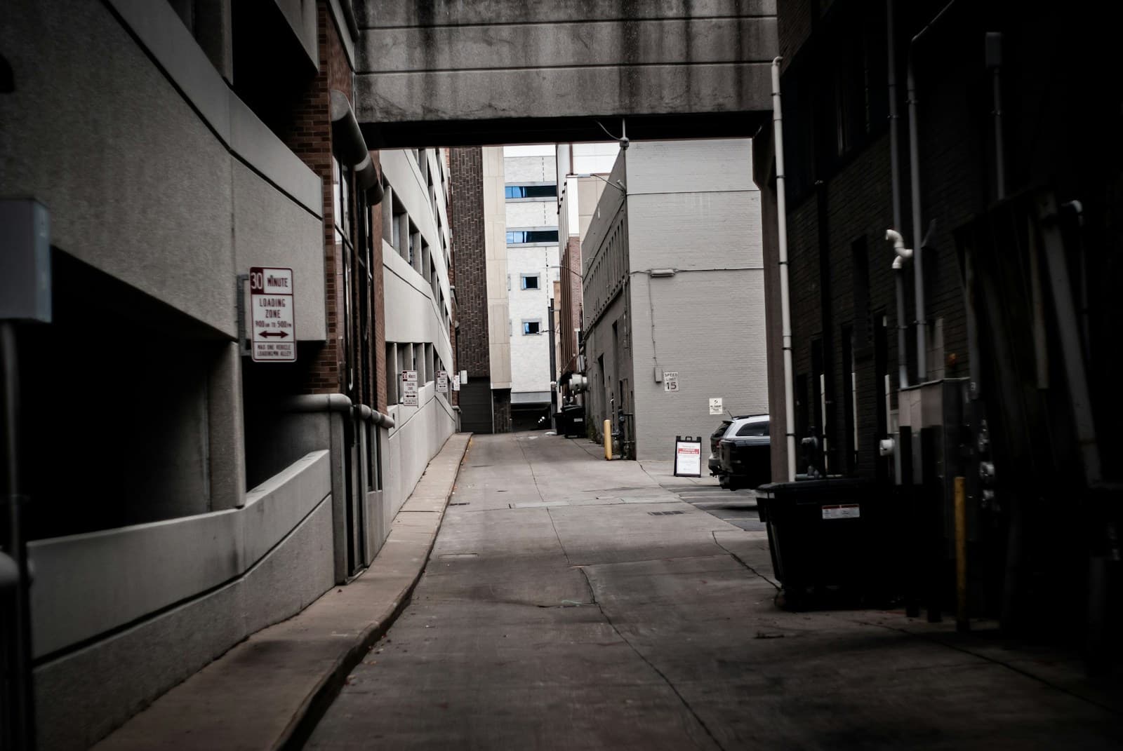 Narrow concrete alleyway between industrial buildings with overcast lighting and urban architecture
