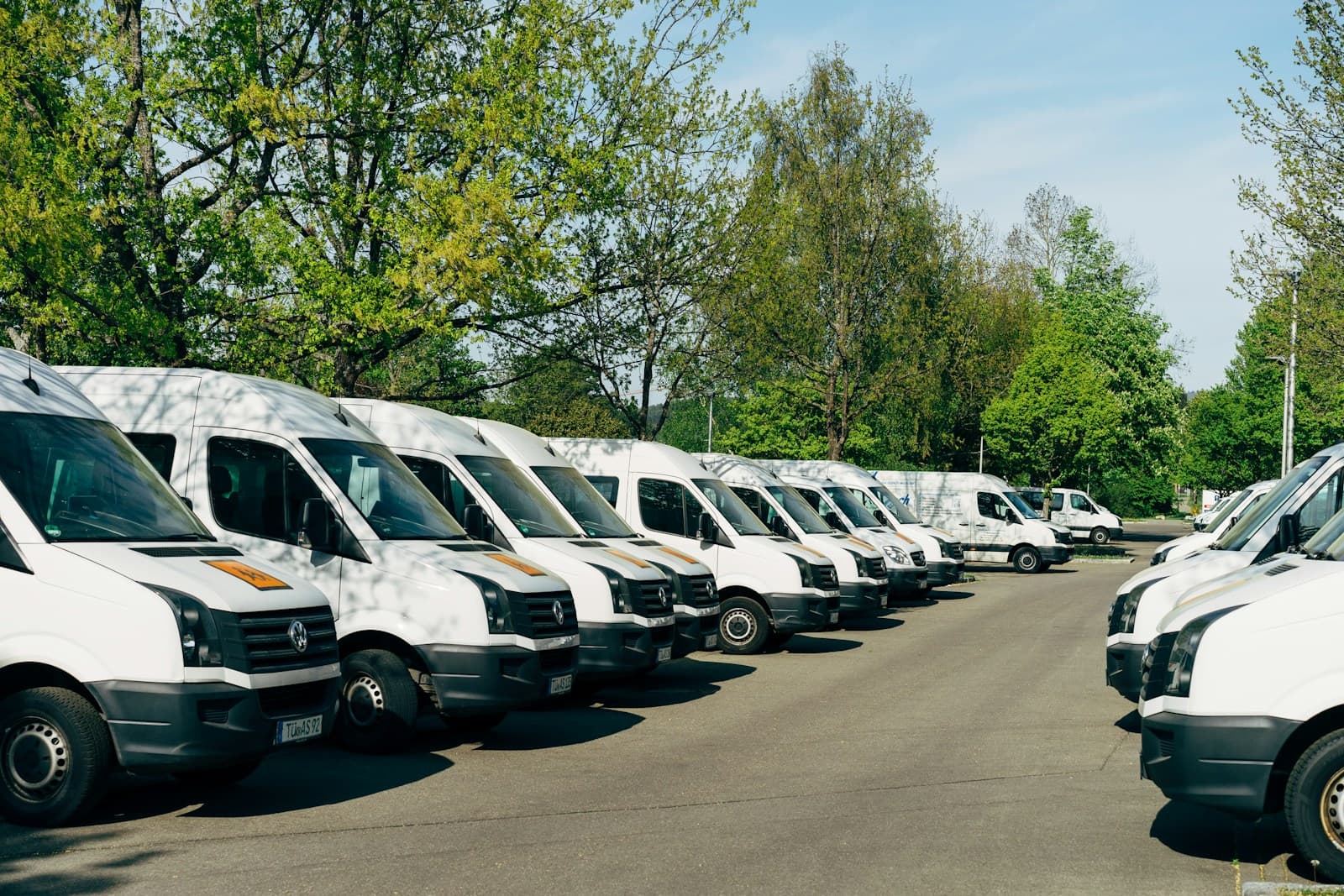 Two rows of white commercial vans parked facing each other on a paved lot
