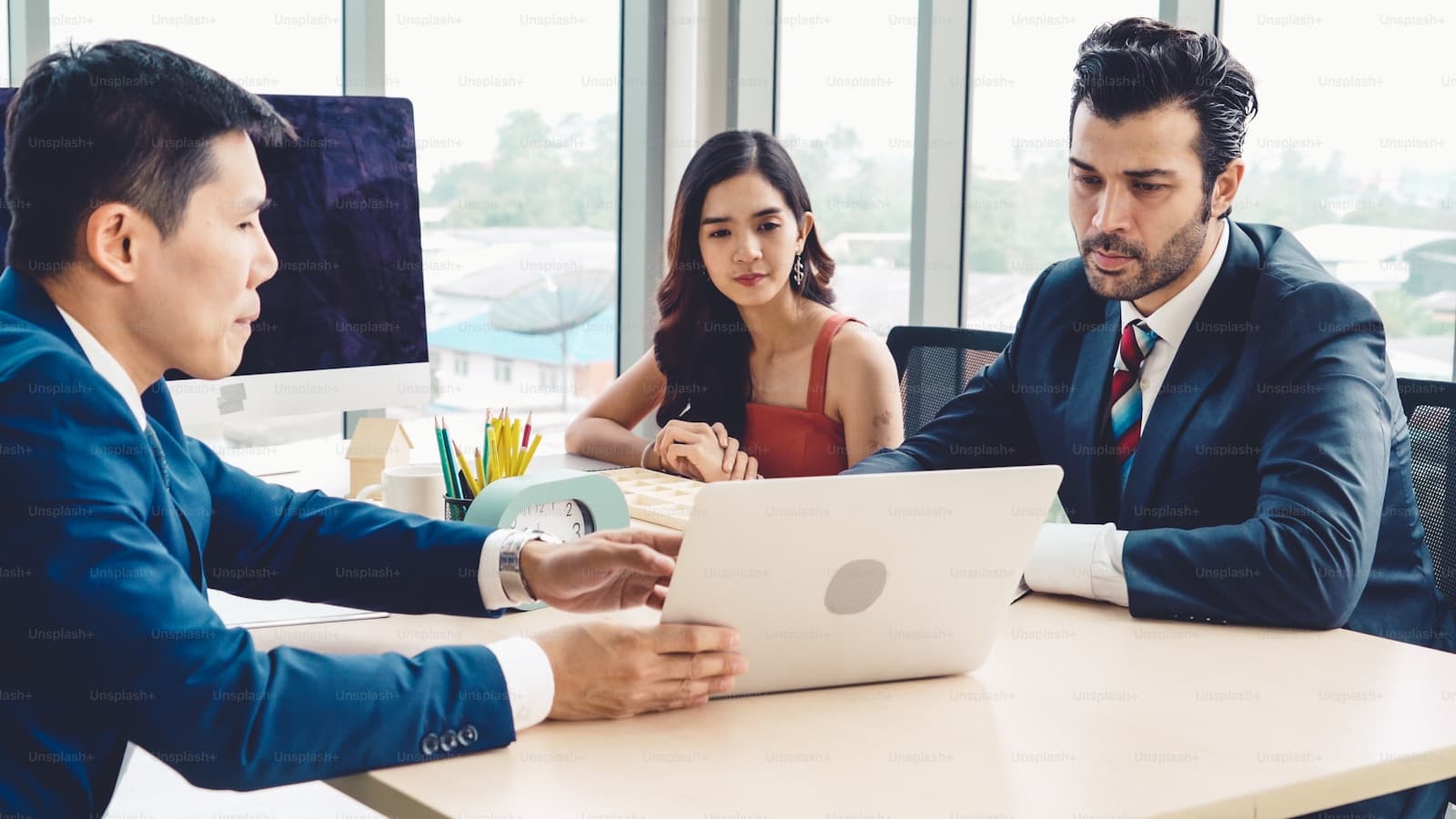 Three professionals meeting at a white table in a sunlit conference room