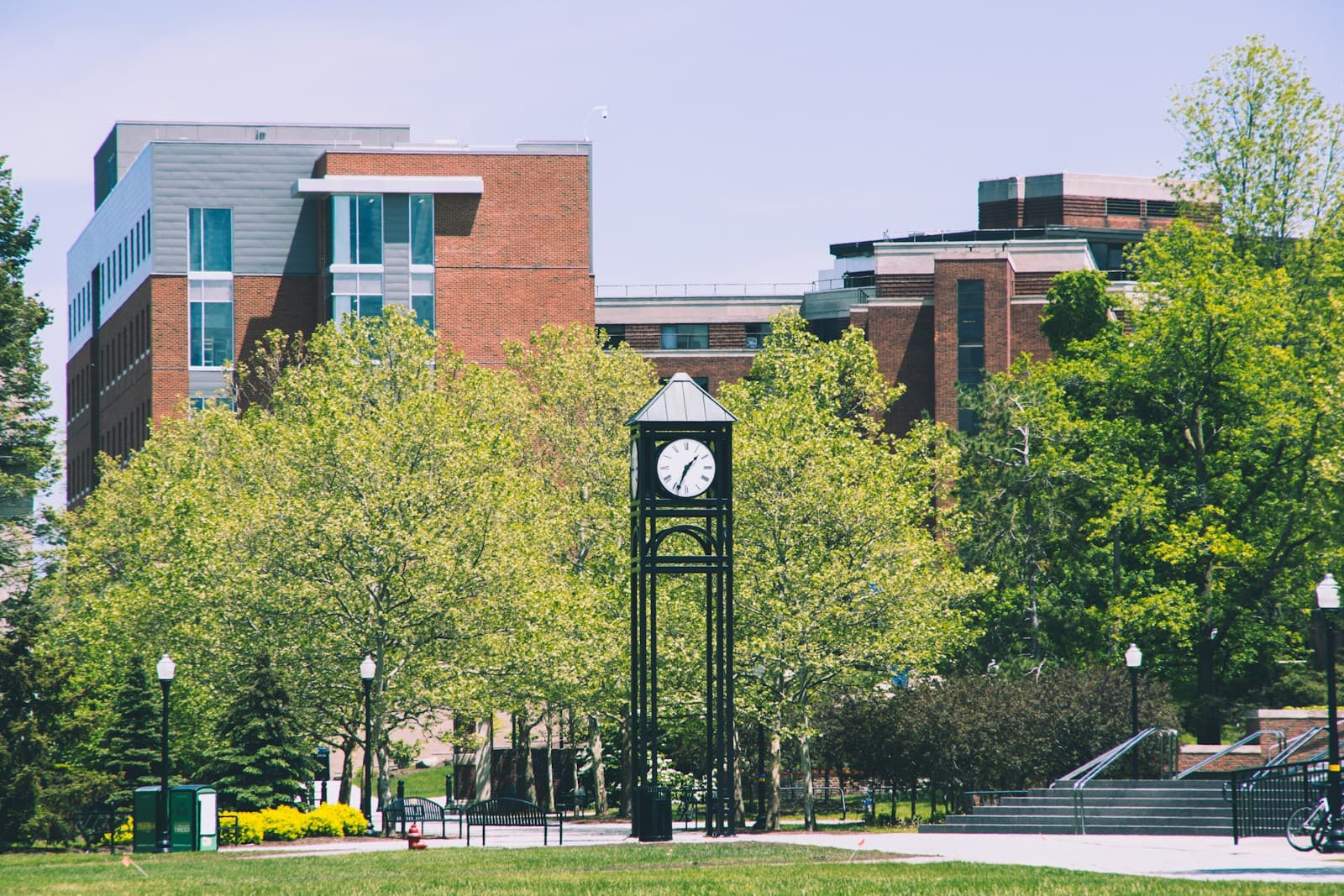 Modern university campus with brick buildings and a black clock tower surrounded by green trees