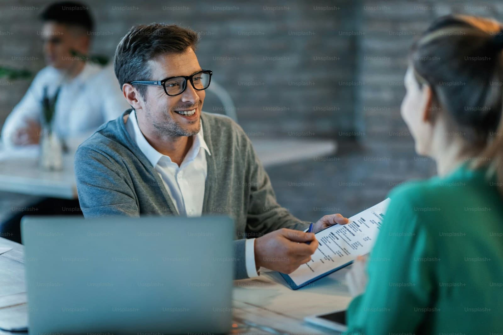 Man in glasses and a cardigan reviewing documents with an agent at an office desk