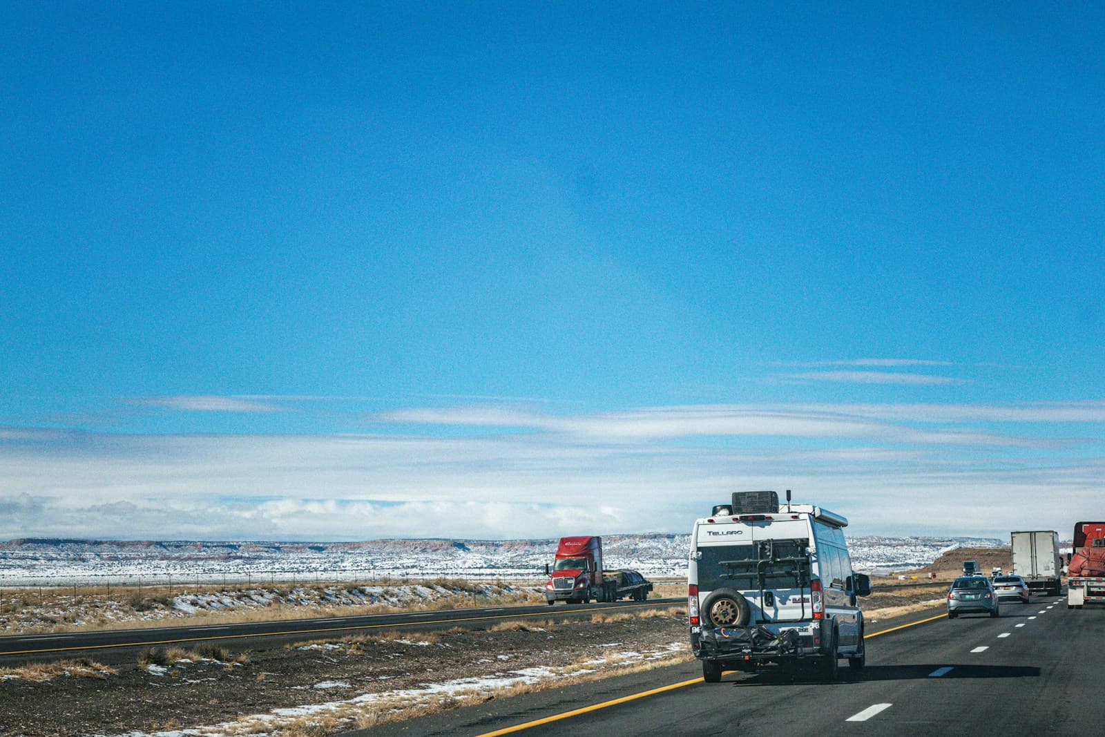 Semi-trucks driving on highway through snowy landscape with blue sky and distant mountains