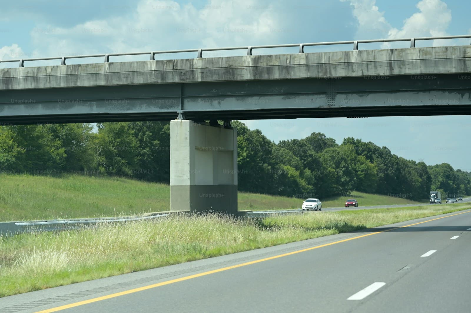Concrete highway overpass bridge crossing over a rural road with grassy fields and trees