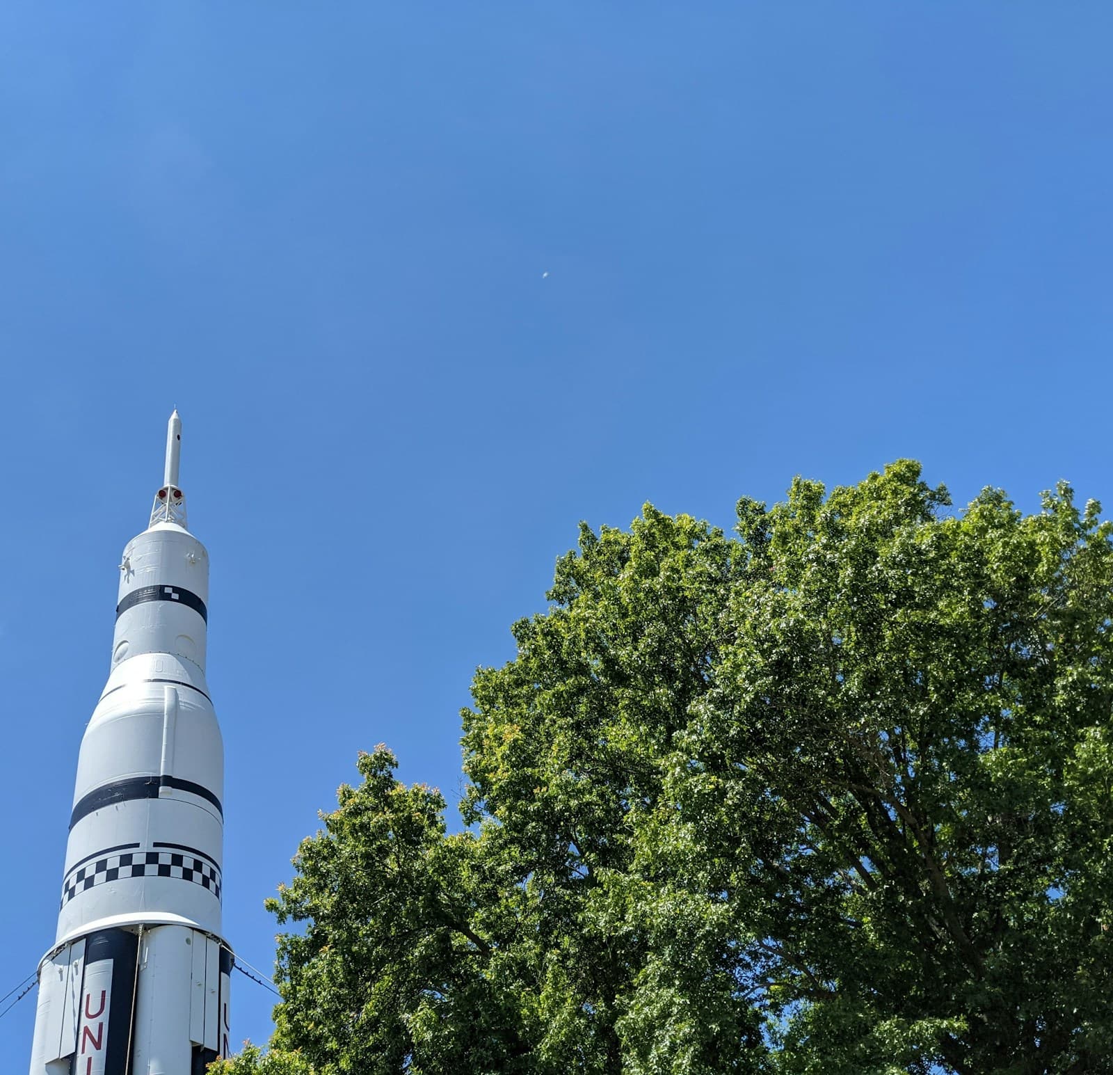 White and black checkered rocket display against blue sky with green trees