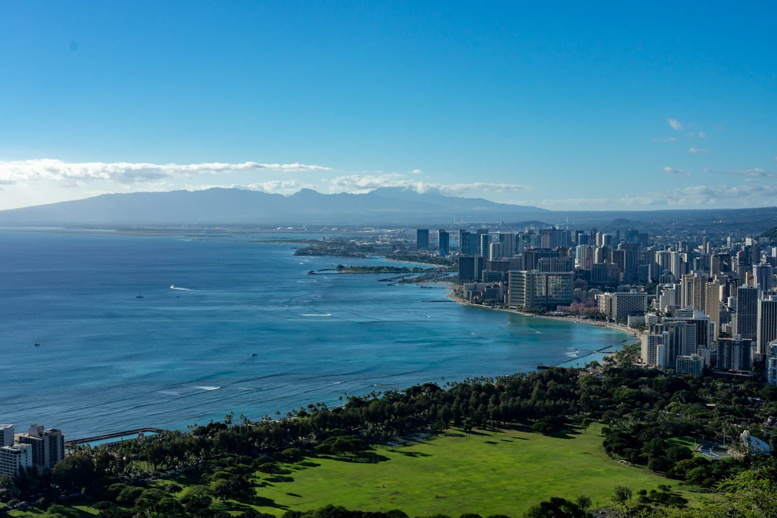 Aerial view of coastal city with high-rise buildings, turquoise bay, beaches, and mountains in background