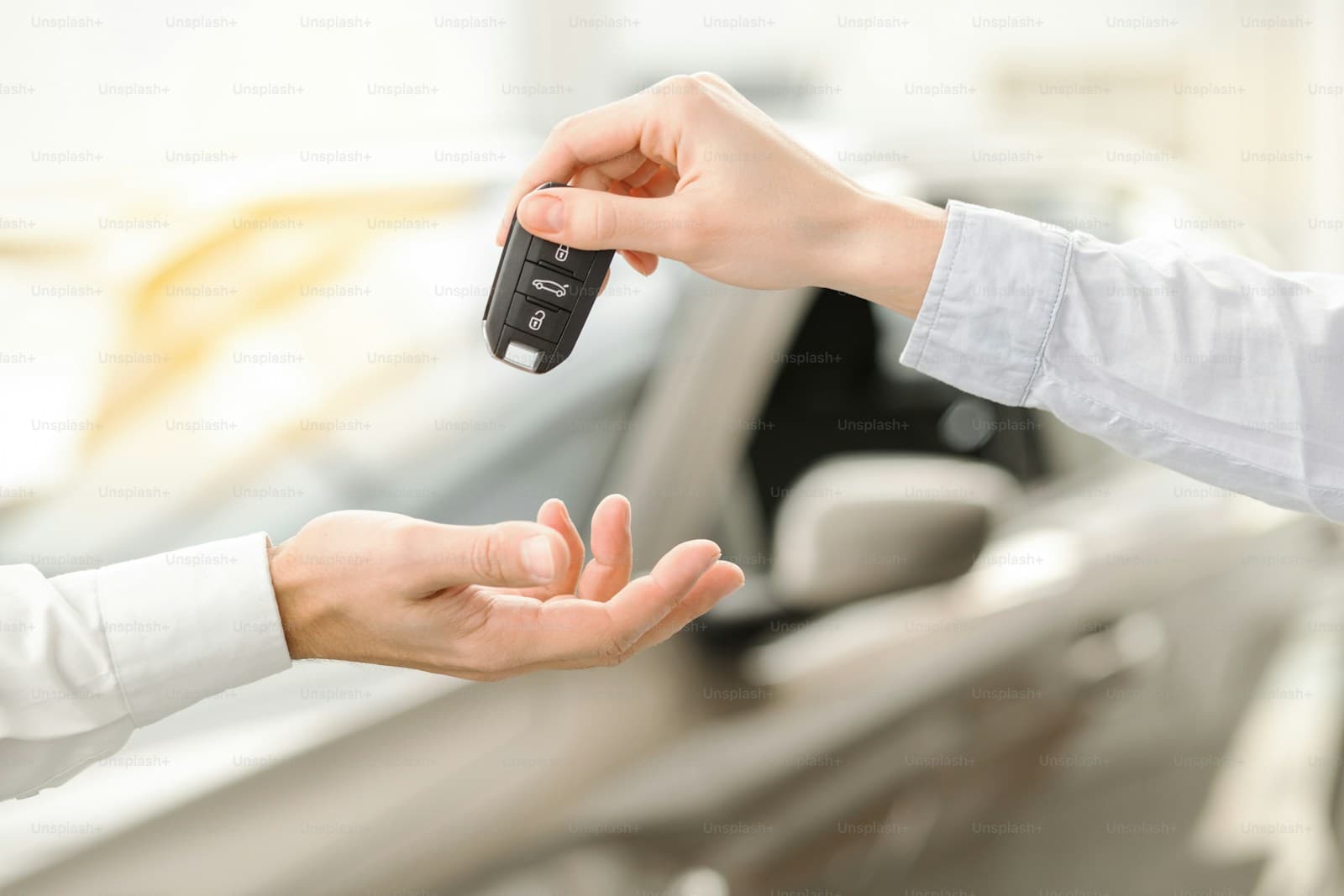 Hands exchanging car keys in front of blurred vehicle background