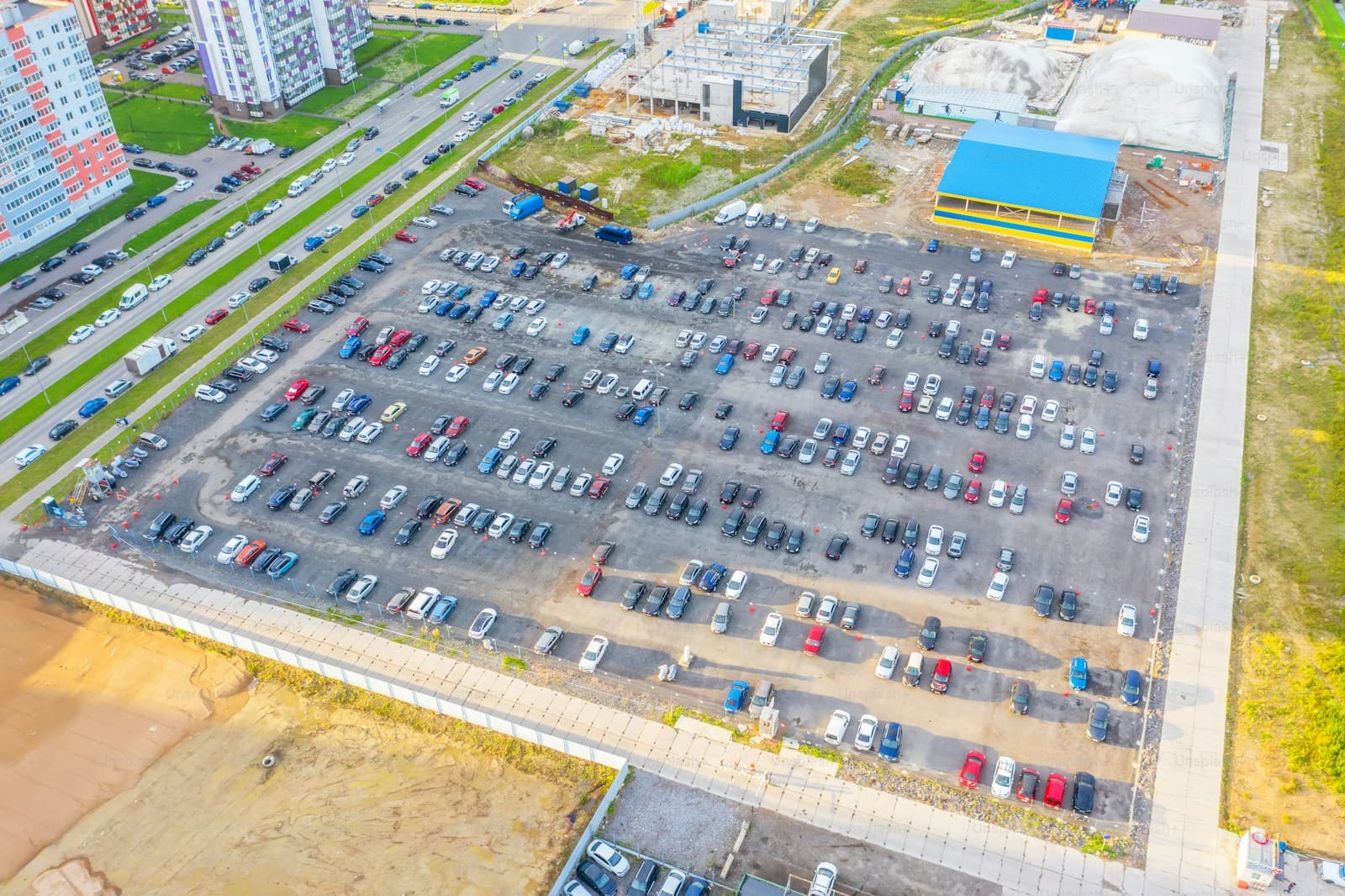 Aerial view of large parking lot filled with cars in organized rows, surrounded by buildings and roads