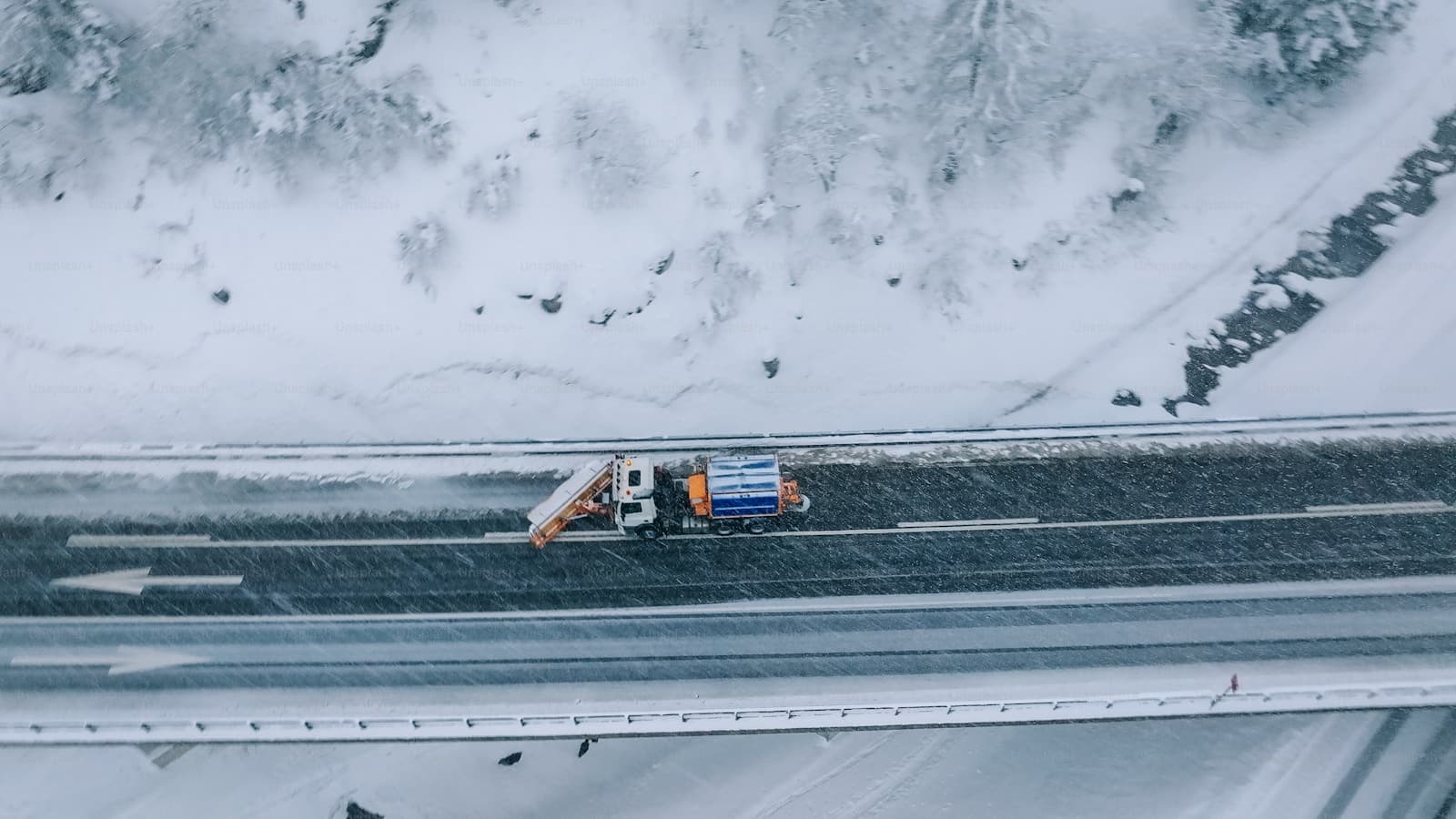 Aerial view of a truck traveling a snow-covered highway between snowy hills