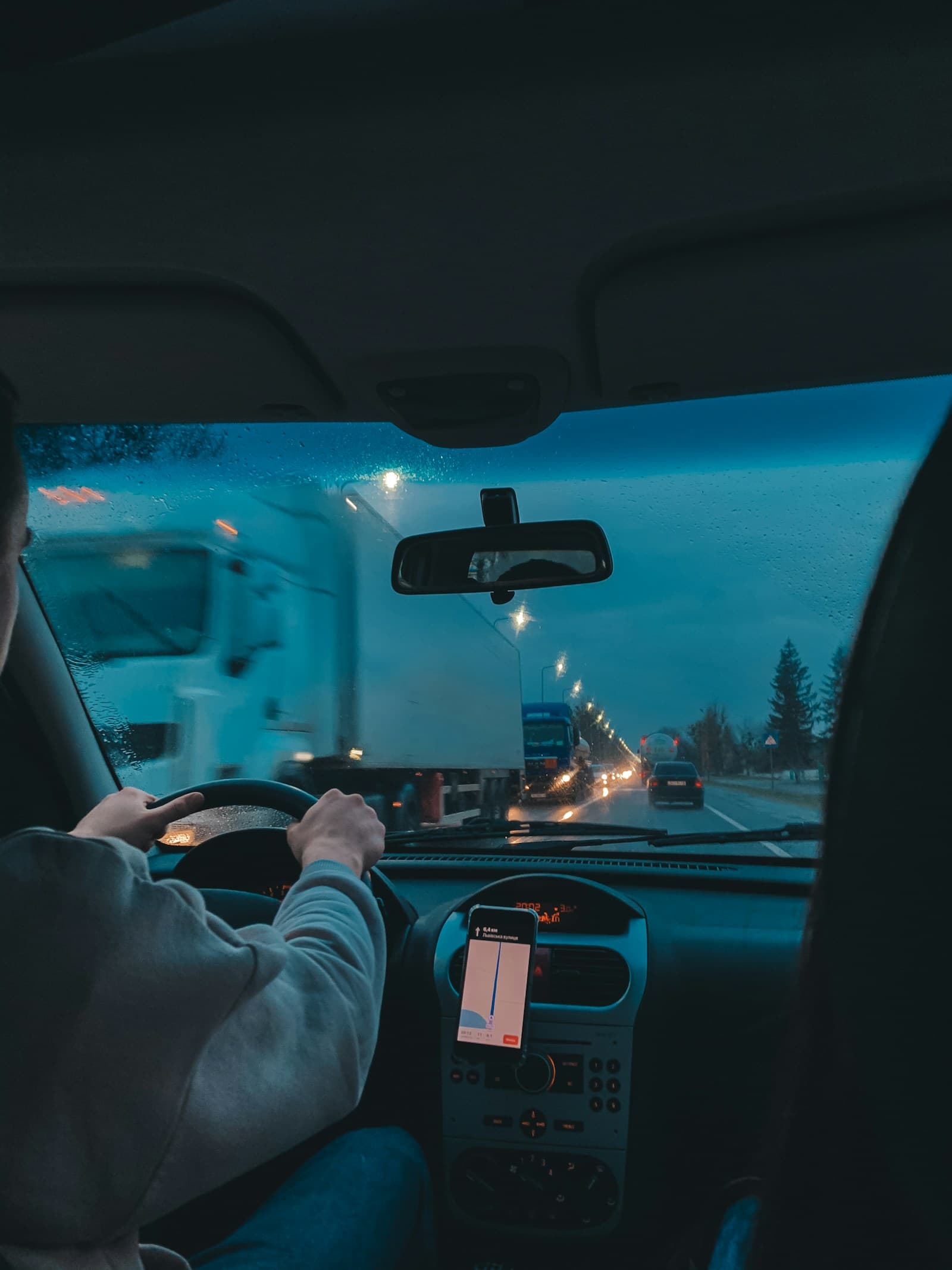 Driver on a snowy highway at twilight with a phone mounted on the dashboard