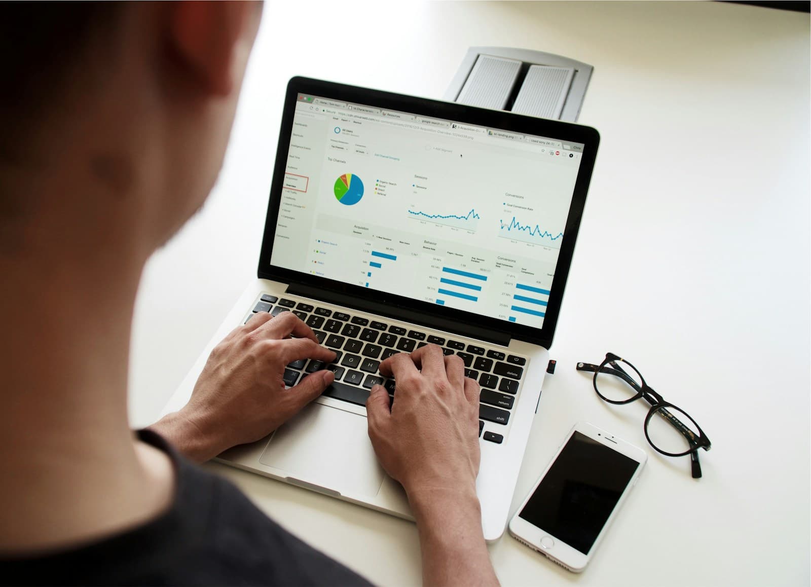 Person typing on a laptop displaying colorful analytics charts at a white desk