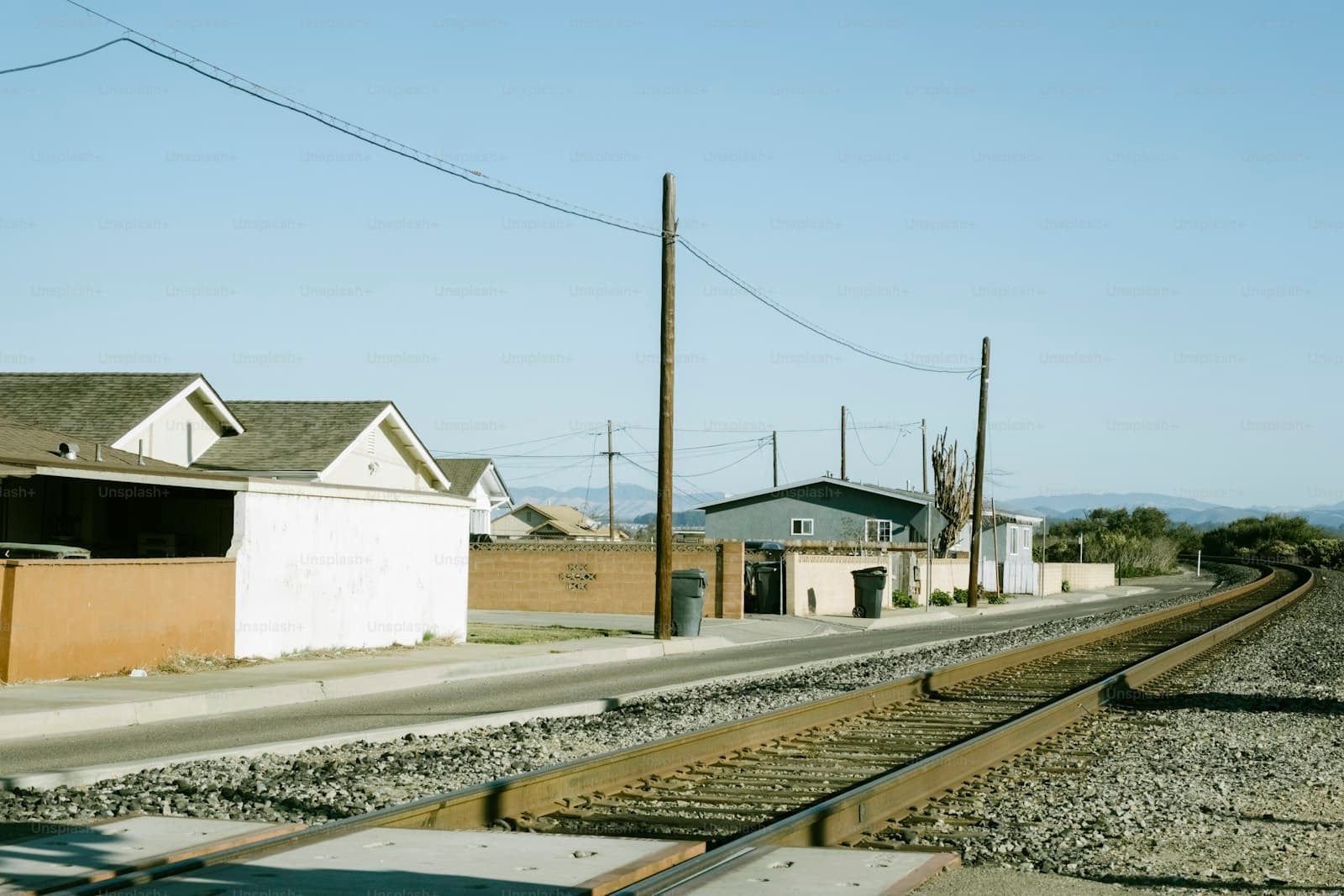Small rural train station building next to railroad tracks with houses and power lines in background