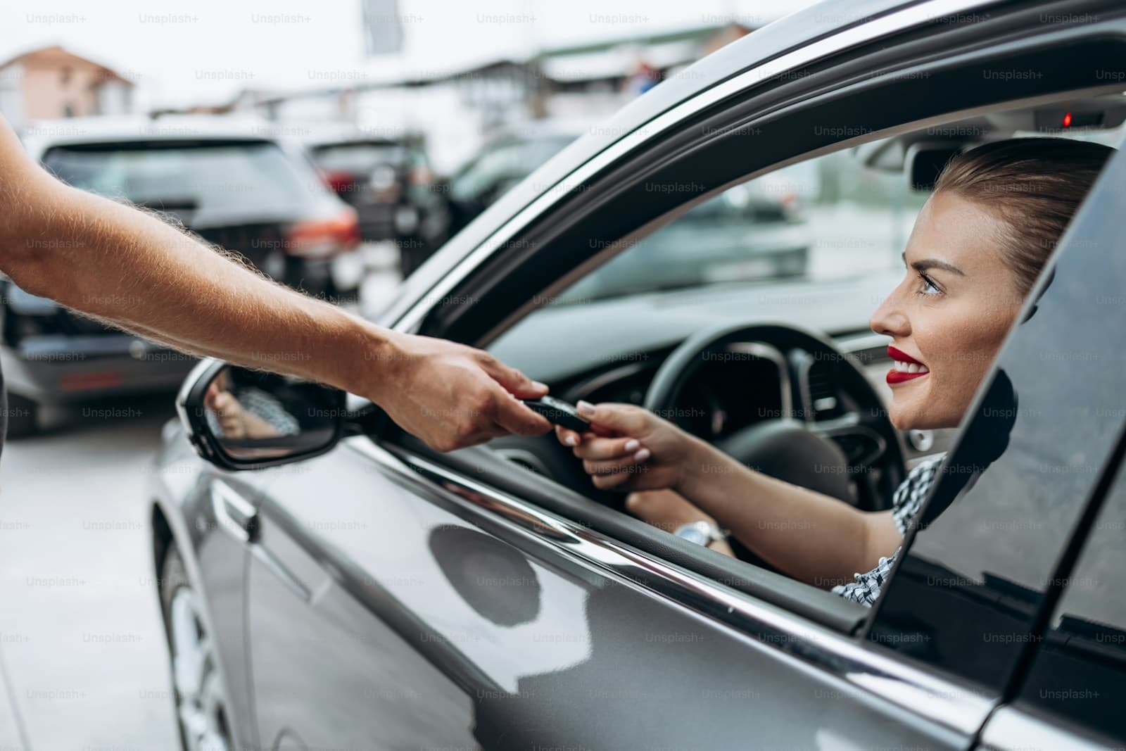 Woman reaching through her car window to accept keys at a dealership lot