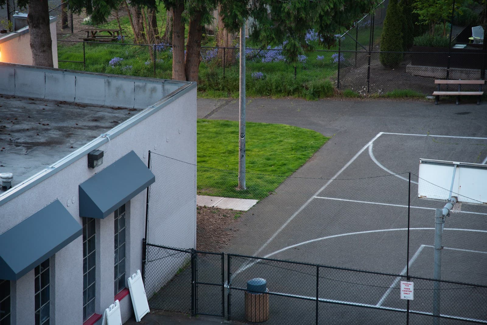 Aerial view of basketball court and school building with fenced recreational area and green lawn
