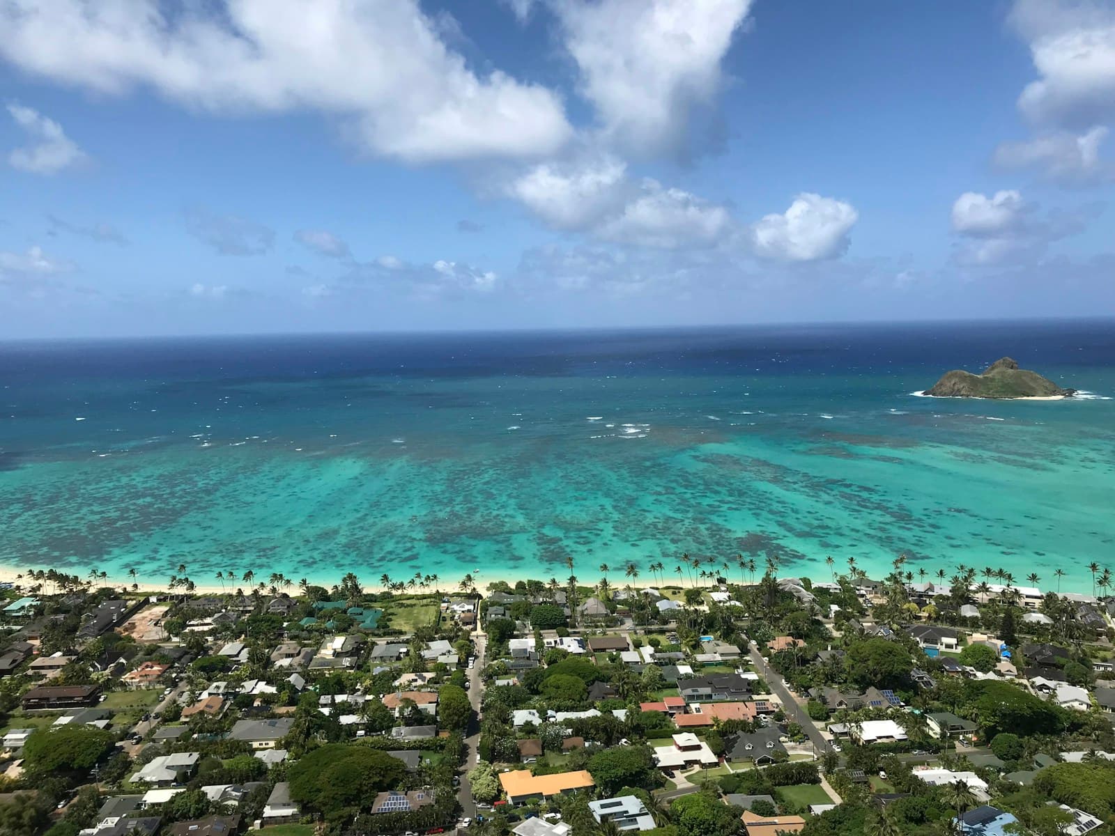 Aerial view of tropical coastal town with turquoise lagoon, white beach, and residential buildings among trees