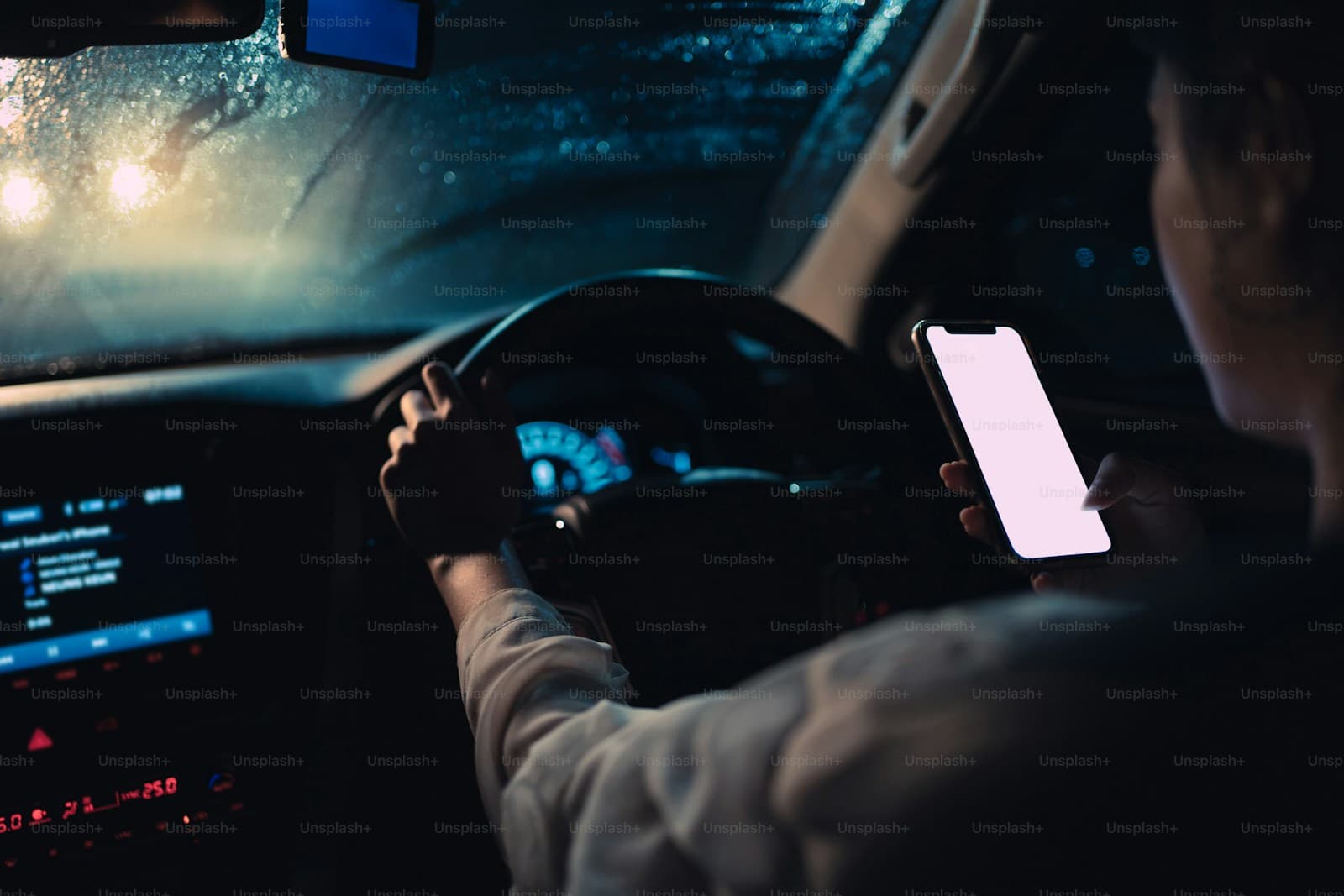 Person driving at night while looking at illuminated smartphone screen, depicting dangerous distracted driving