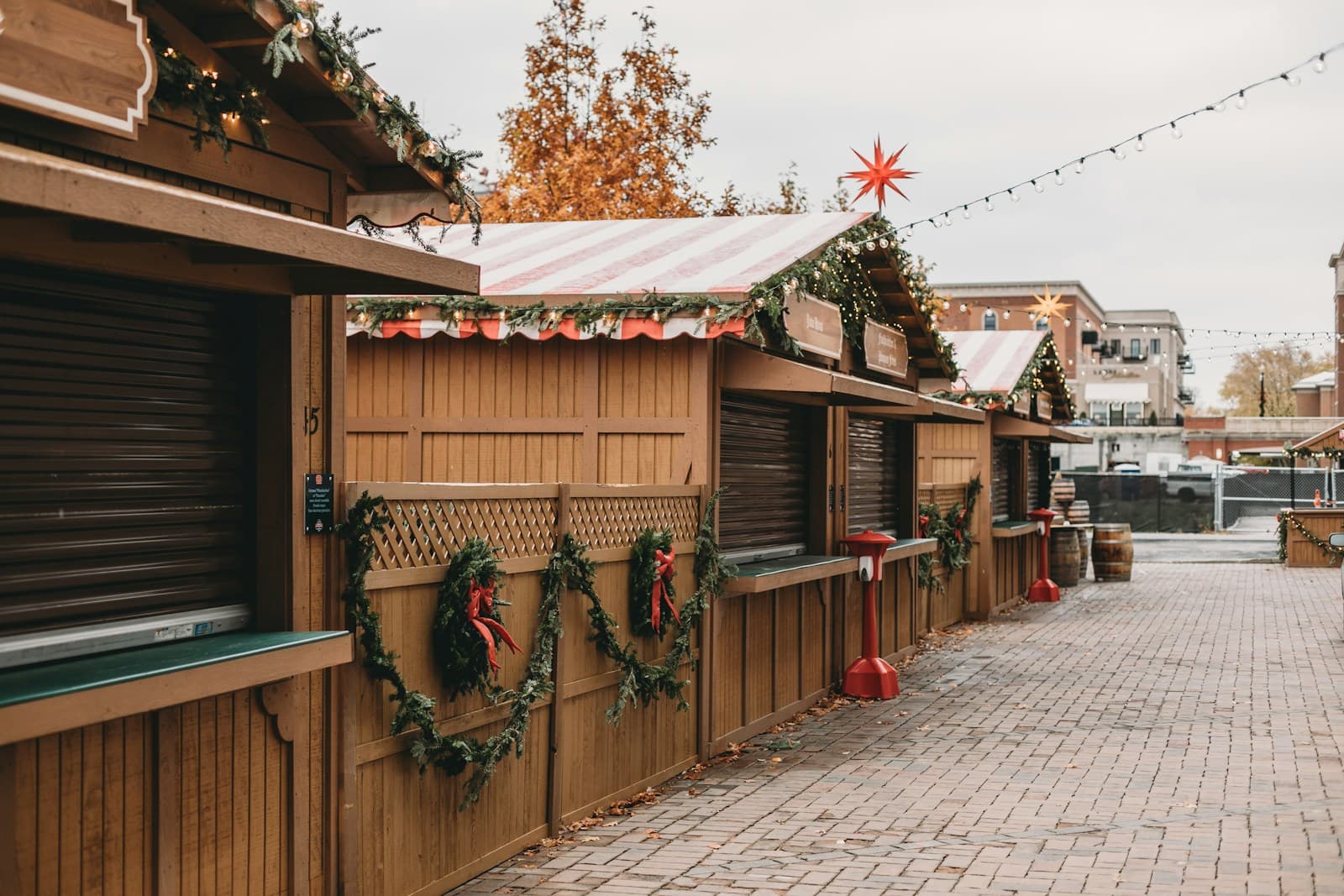 Wooden Christmas market stalls decorated with holiday garlands and lights on a brick plaza