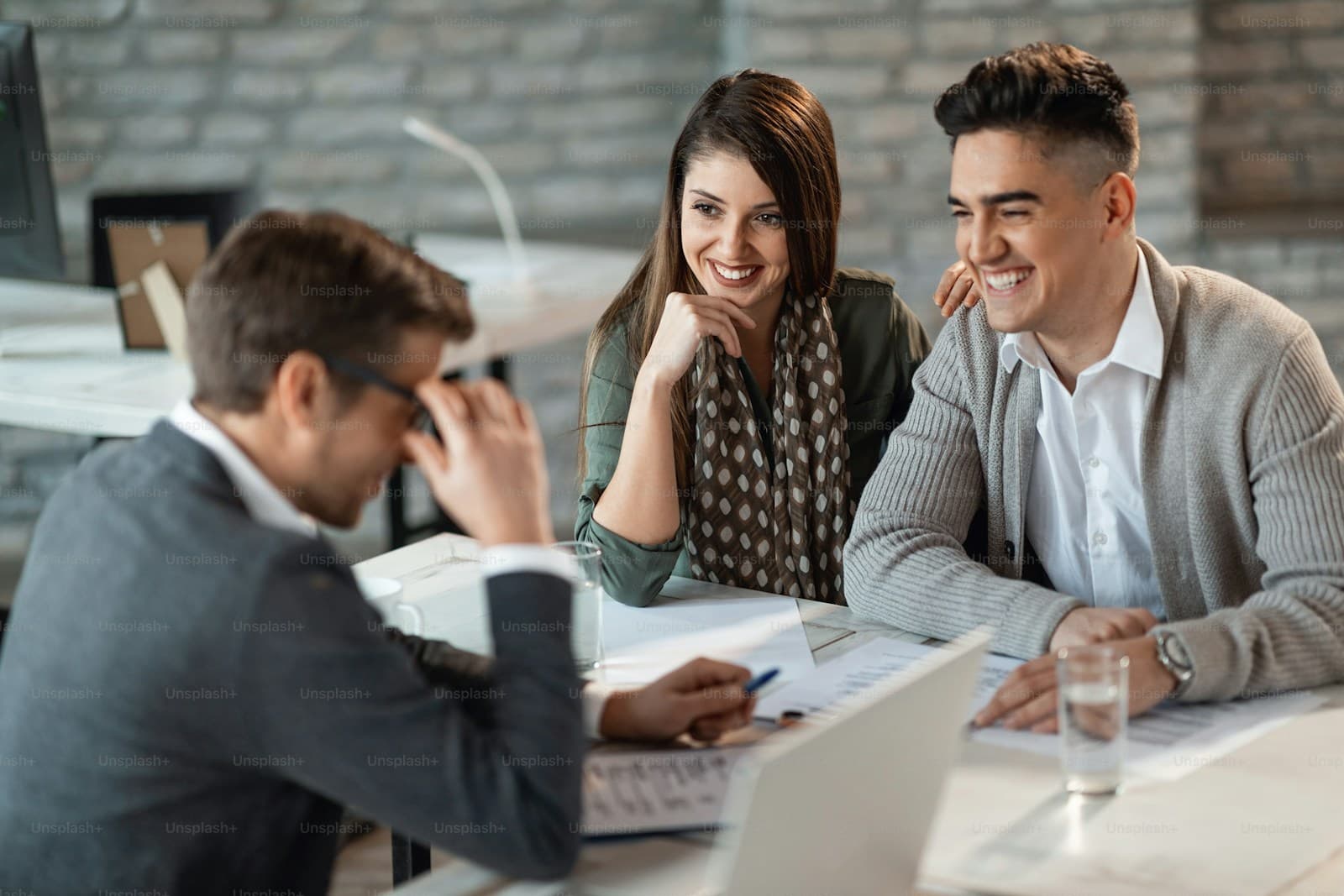 Adviser in a dark suit reviewing documents with a smiling couple at a modern table