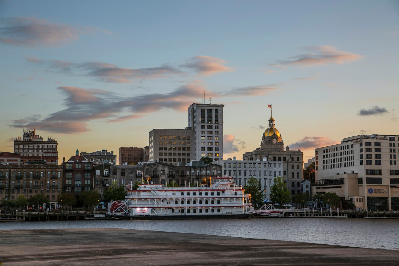 Historic paddle wheel steamboat docked at waterfront with city skyline and domed building at sunset