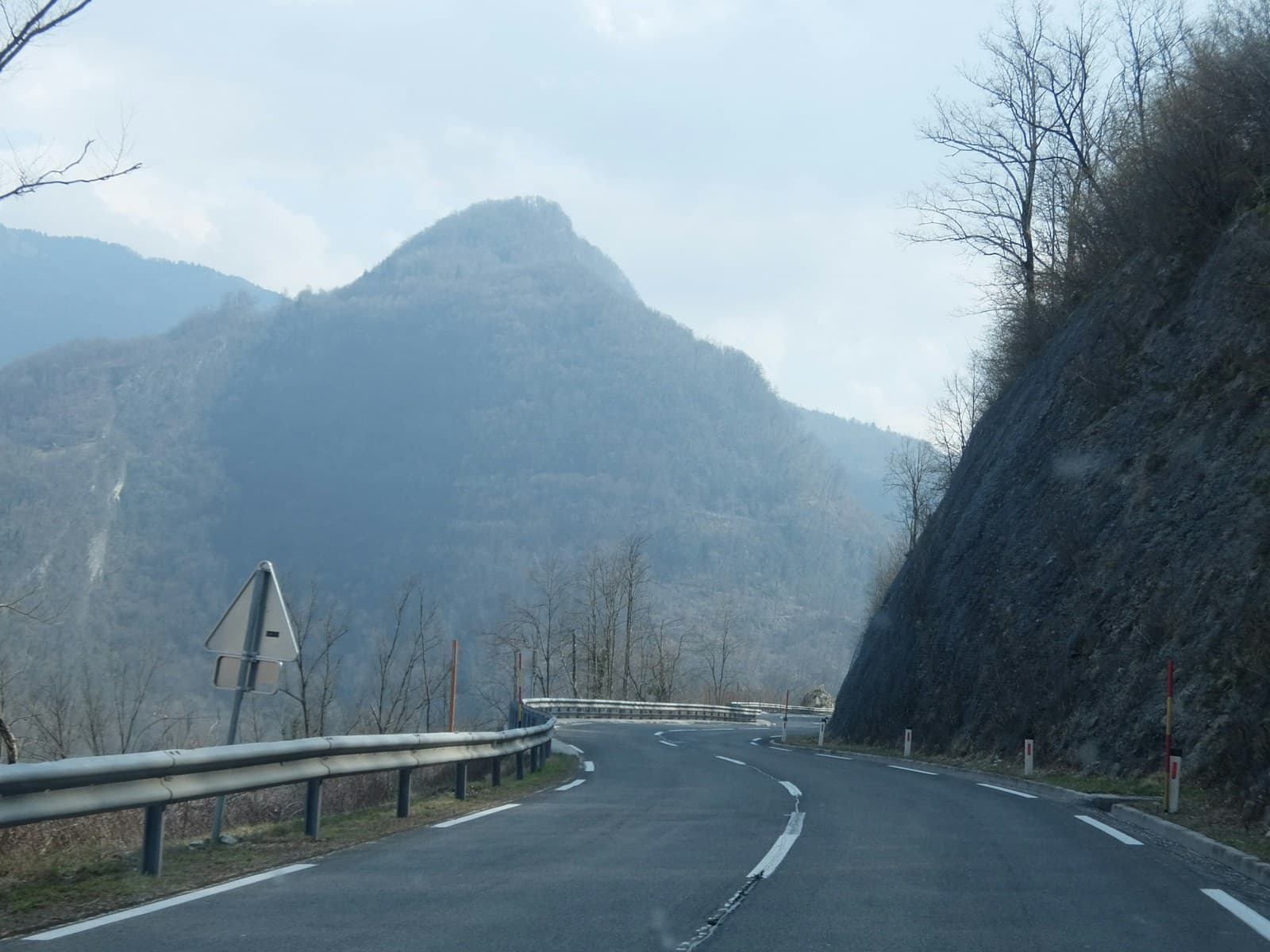Empty winding mountain highway with guardrails curving through a valley under an overcast sky