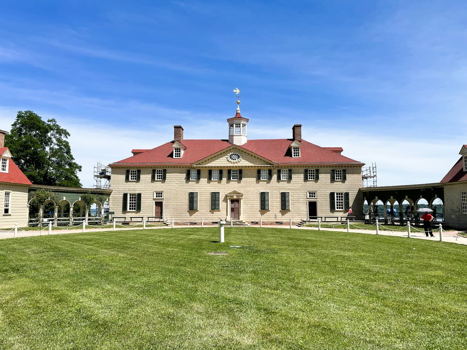 Historic colonial mansion with red roof and cream stone walls on green lawn under blue sky