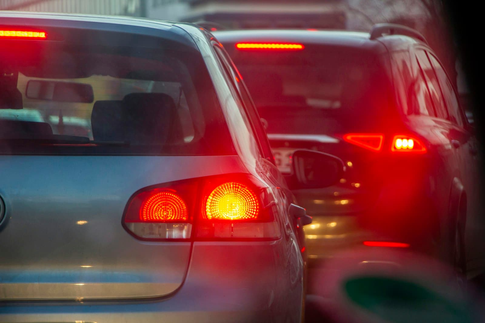 Cars in traffic with red brake lights and taillights glowing in low light conditions
