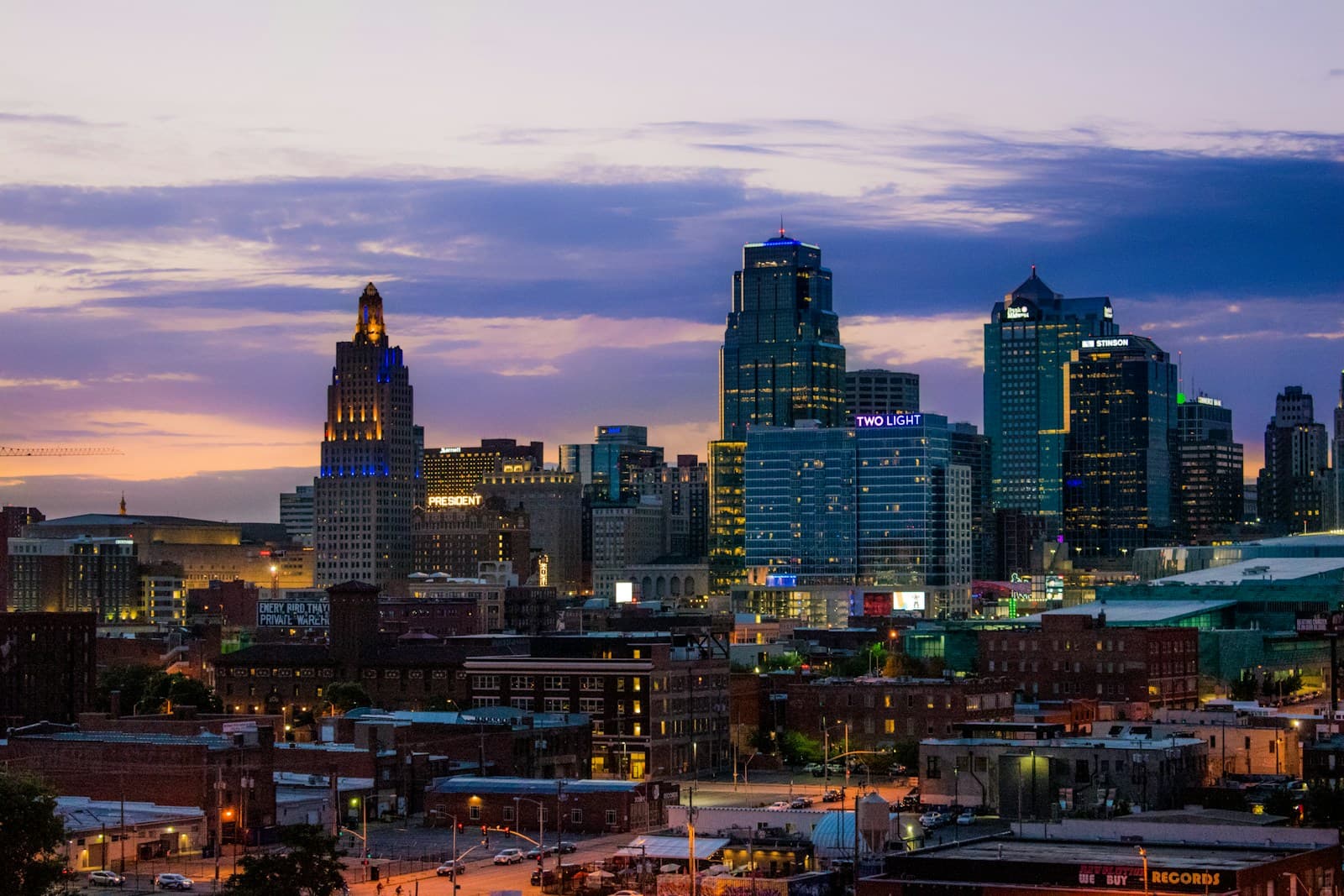 Downtown city skyline at dusk with illuminated skyscrapers against purple sunset sky