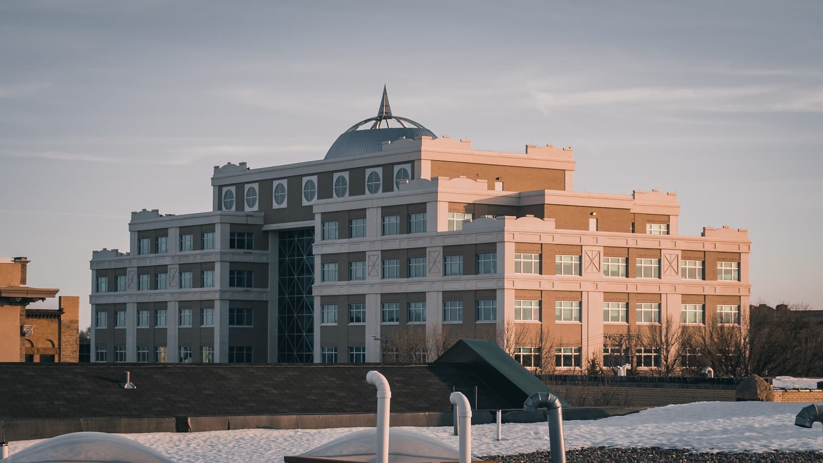 Modern multi-story building complex with curved dome feature and mixed facade colors during golden hour lighting